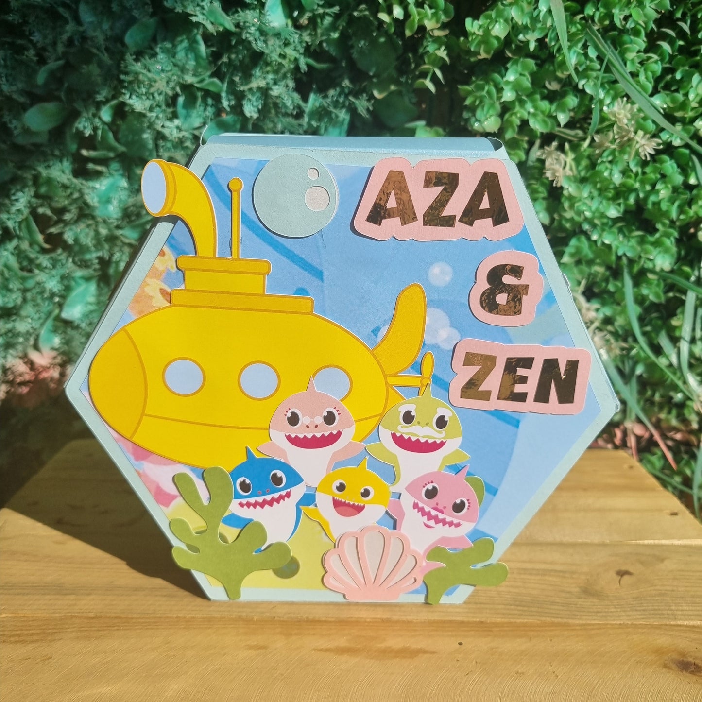 Hexagonal children's nameplate with cartoon characters and 'Aza & Zen' text, placed outdoors.