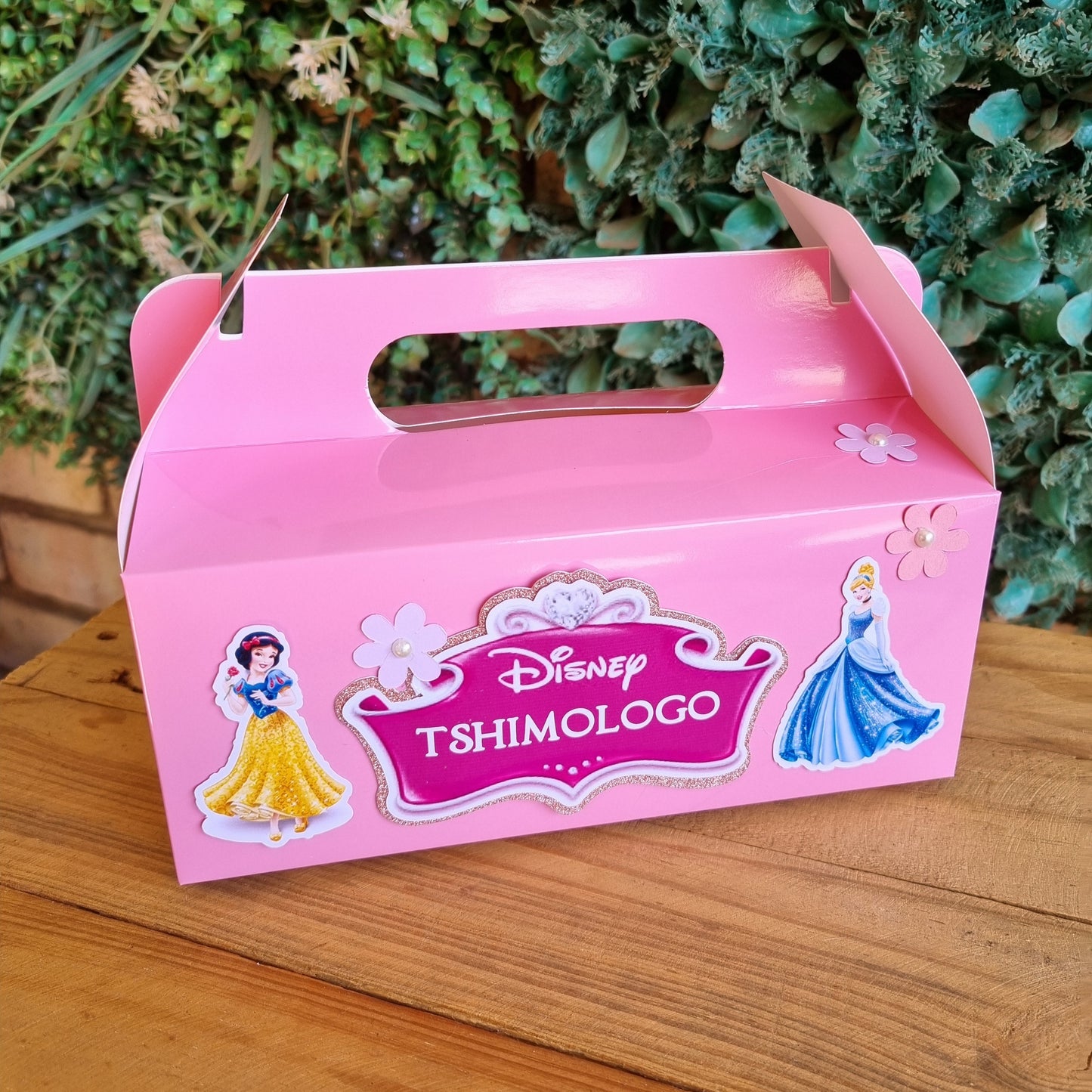 Pink box with Disney Tsum Tsum logo on a wooden surface with greenery in the background