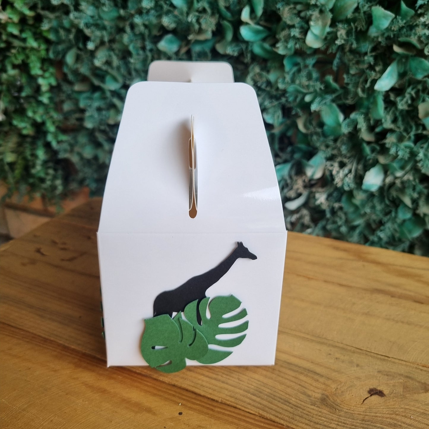 White paper with black and green cut-out shapes on a wooden surface with green foliage in the background