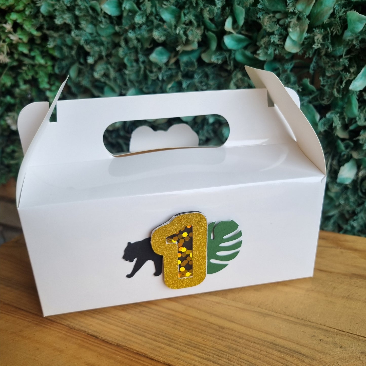 White gift box with a decorative design on a wooden surface and green foliage background