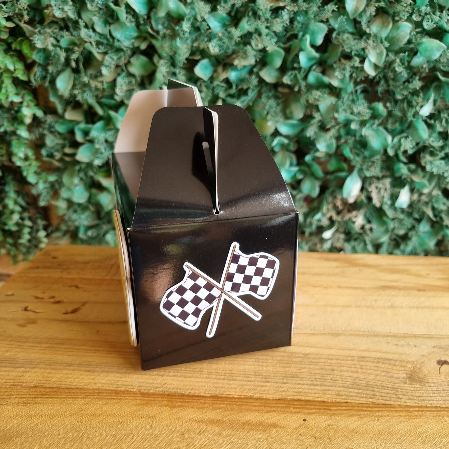 Black metal object with checkered patterns attached to a wooden surface and green foliage background