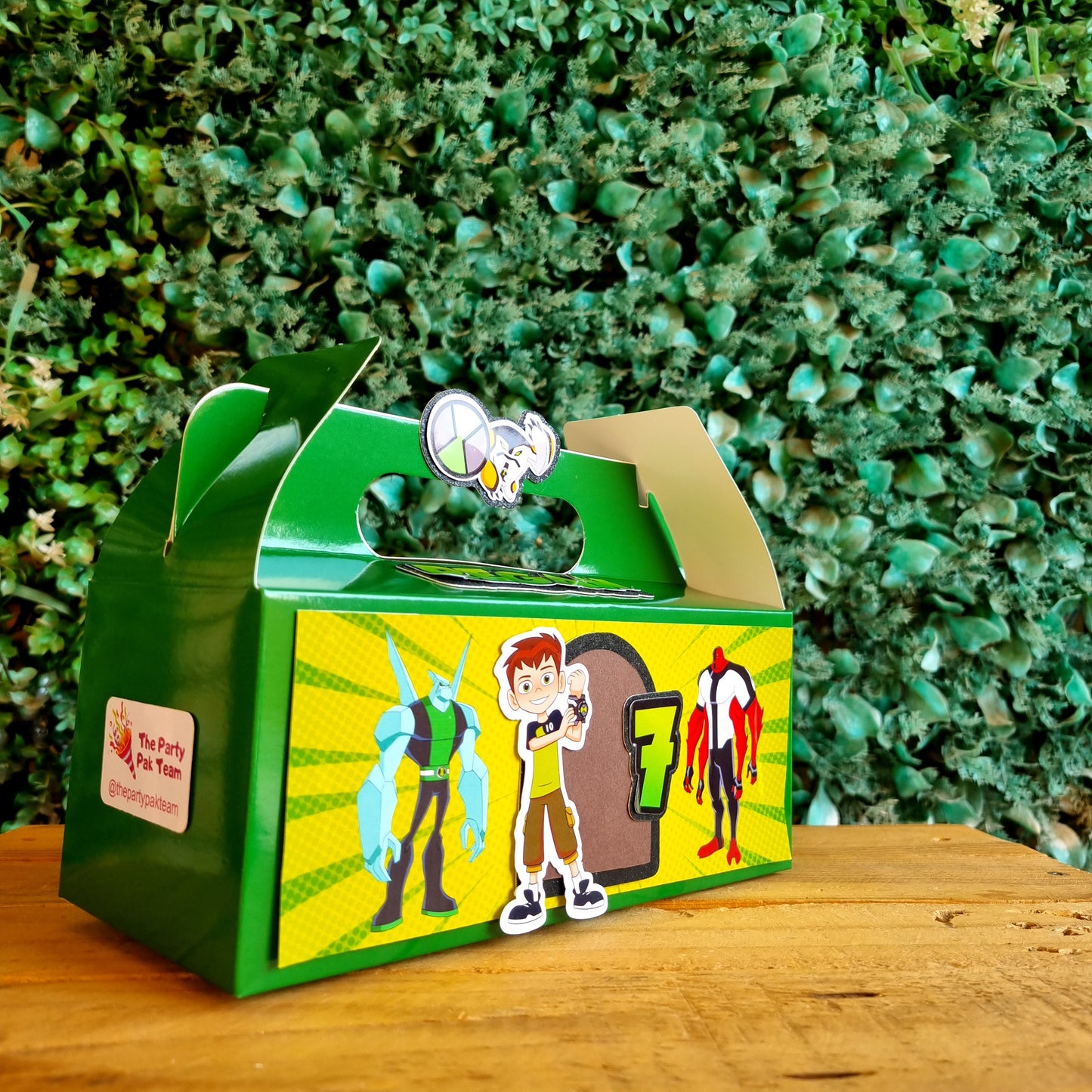 Cartoon character box with a green base on a wooden surface and green plants in the background
