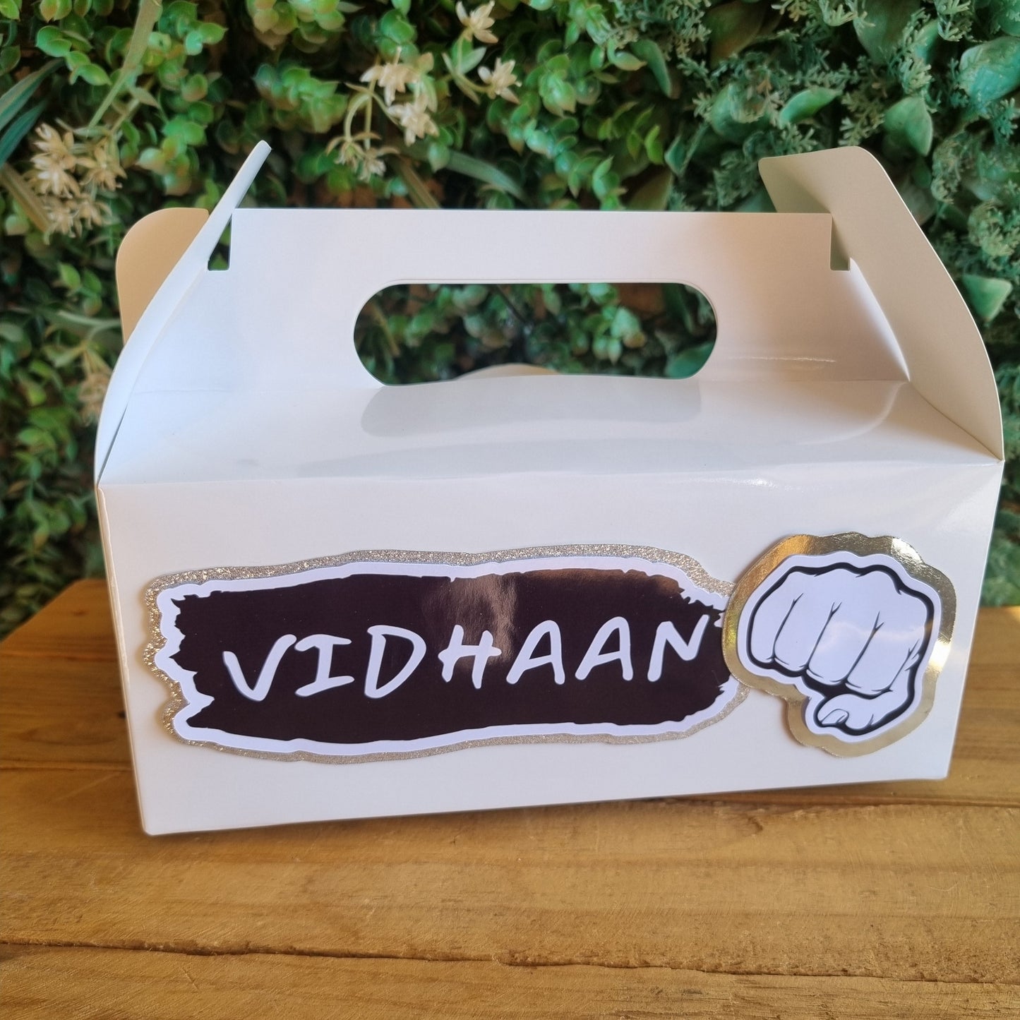 Small cardboard box with 'VIDHAAN' branding on a wooden surface with greenery in the background