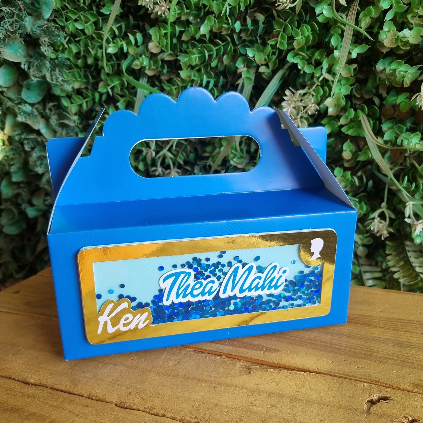 Blue toy truck with 'Ken' branding on a wooden surface and greenery background