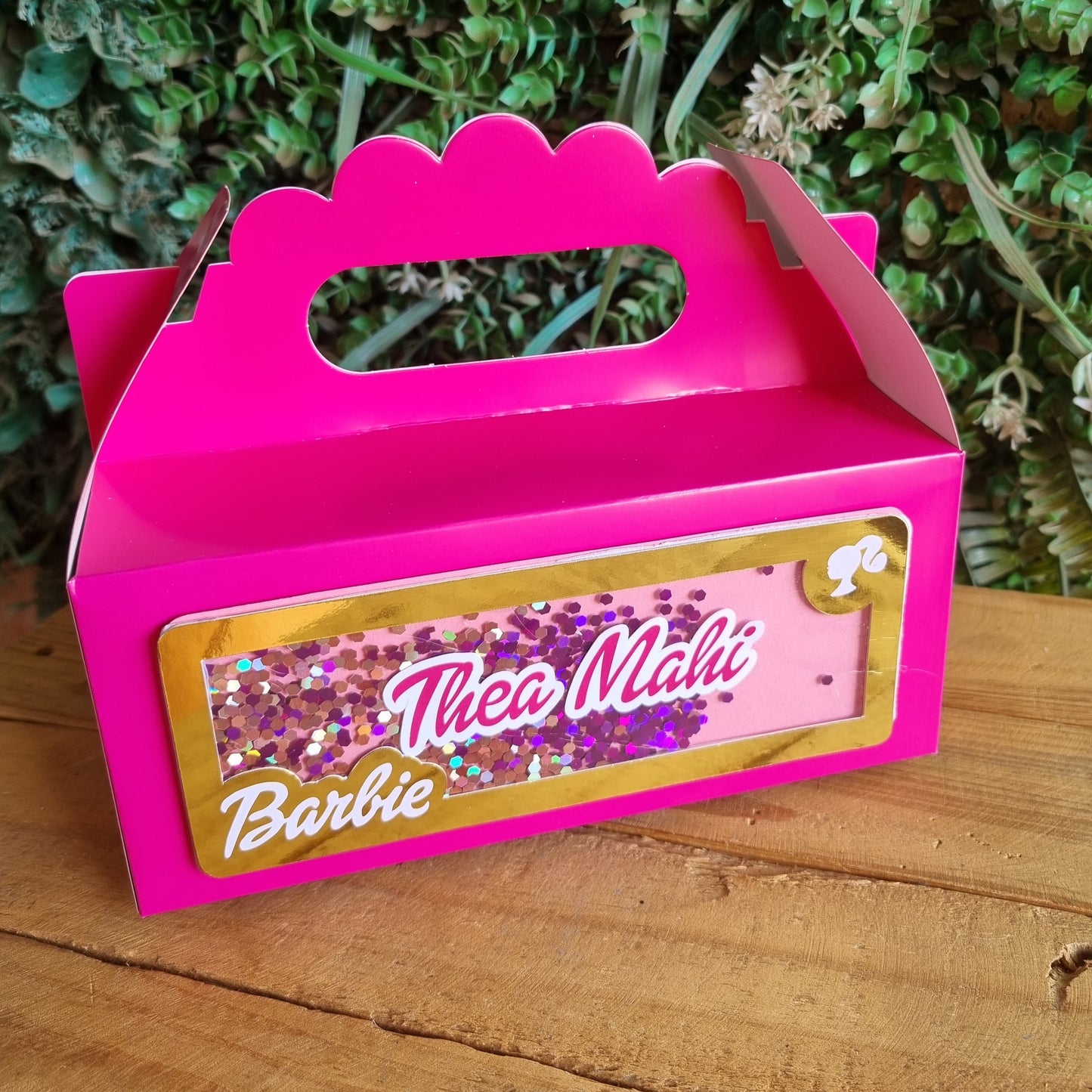 Pink toy box with 'Barbie' branding on a wooden surface and grass background