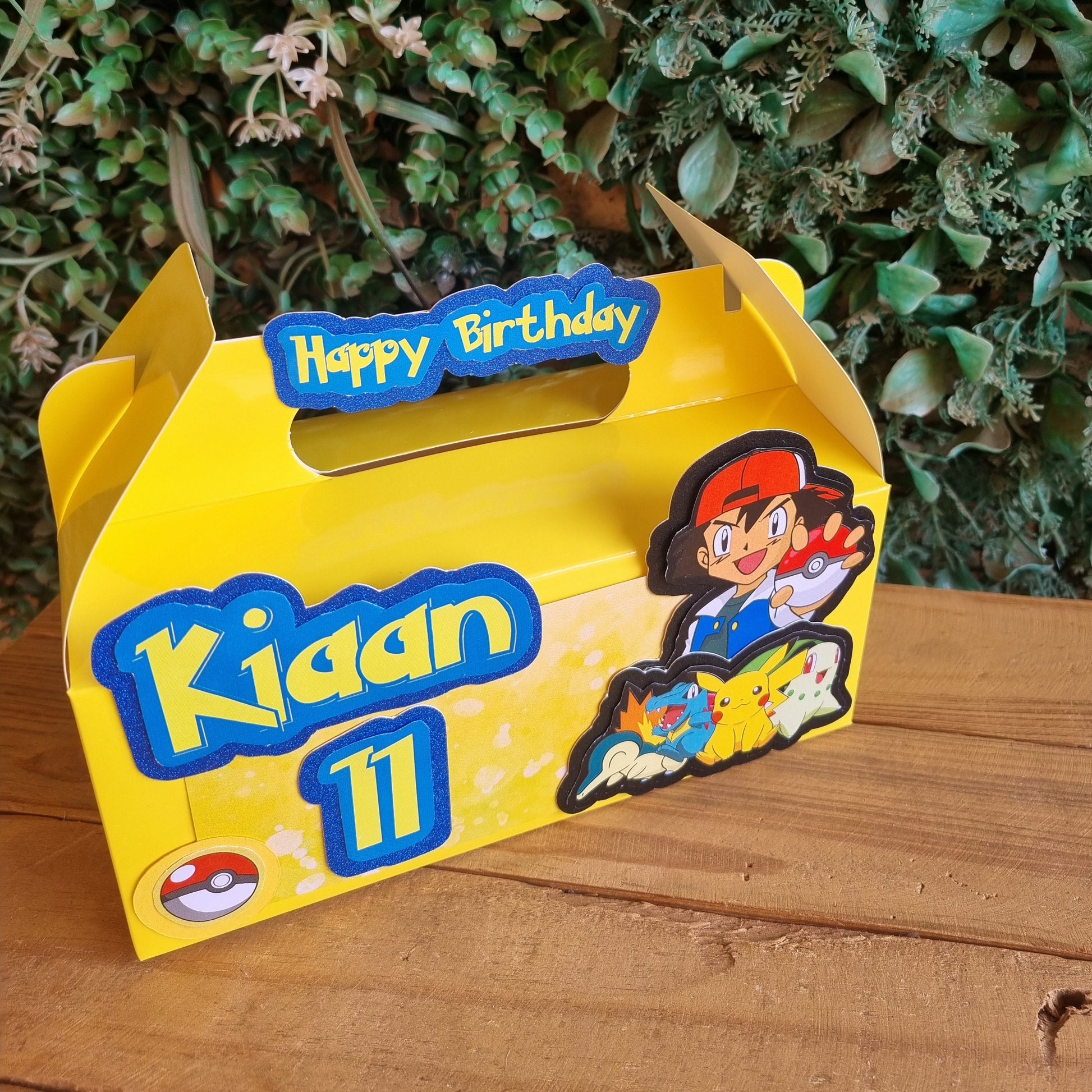 Yellow toy box with cartoon characters on a wooden surface and green plants in the background
