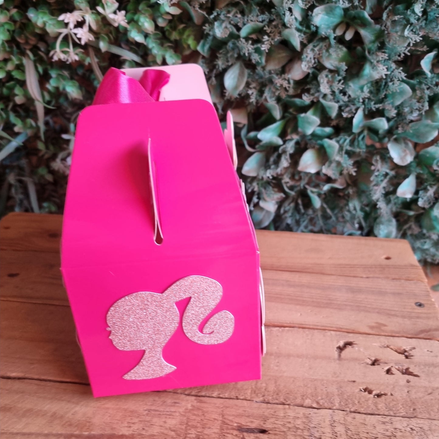 Pink flamingo-shaped object on a wooden surface with greenery in the background
