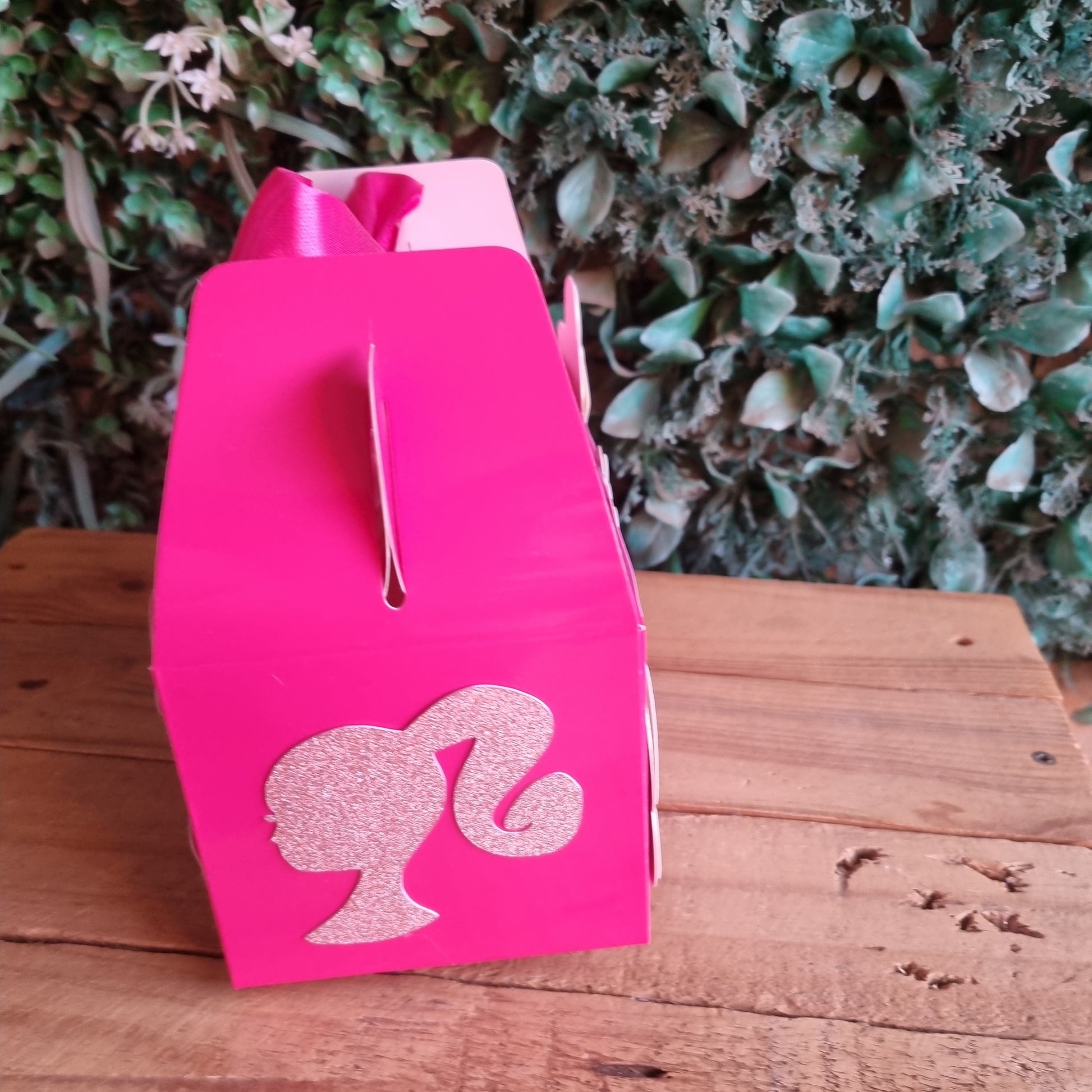 Pink flamingo-shaped object on a wooden surface with greenery in the background