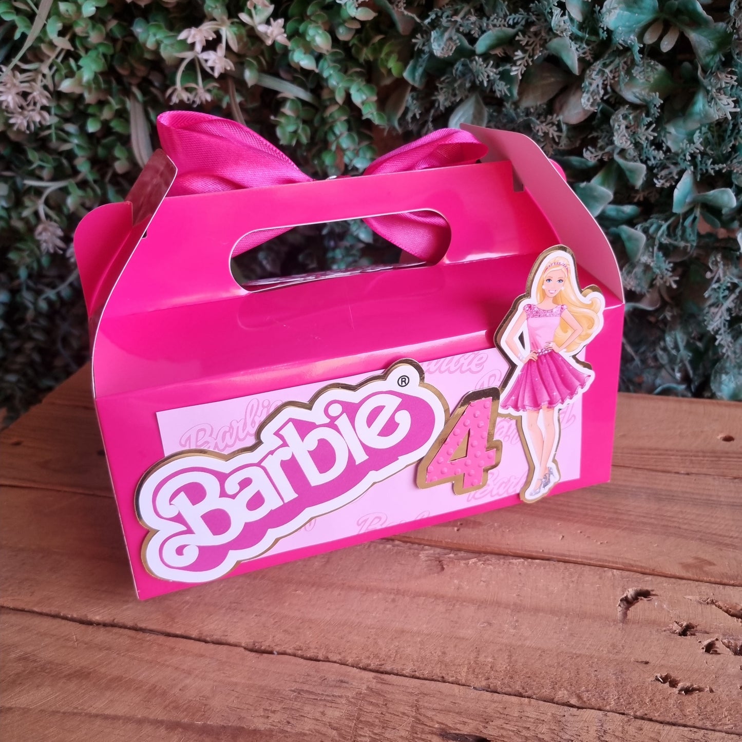 Pink toy box with a bow and 'Barbie' branding on a wooden surface.
