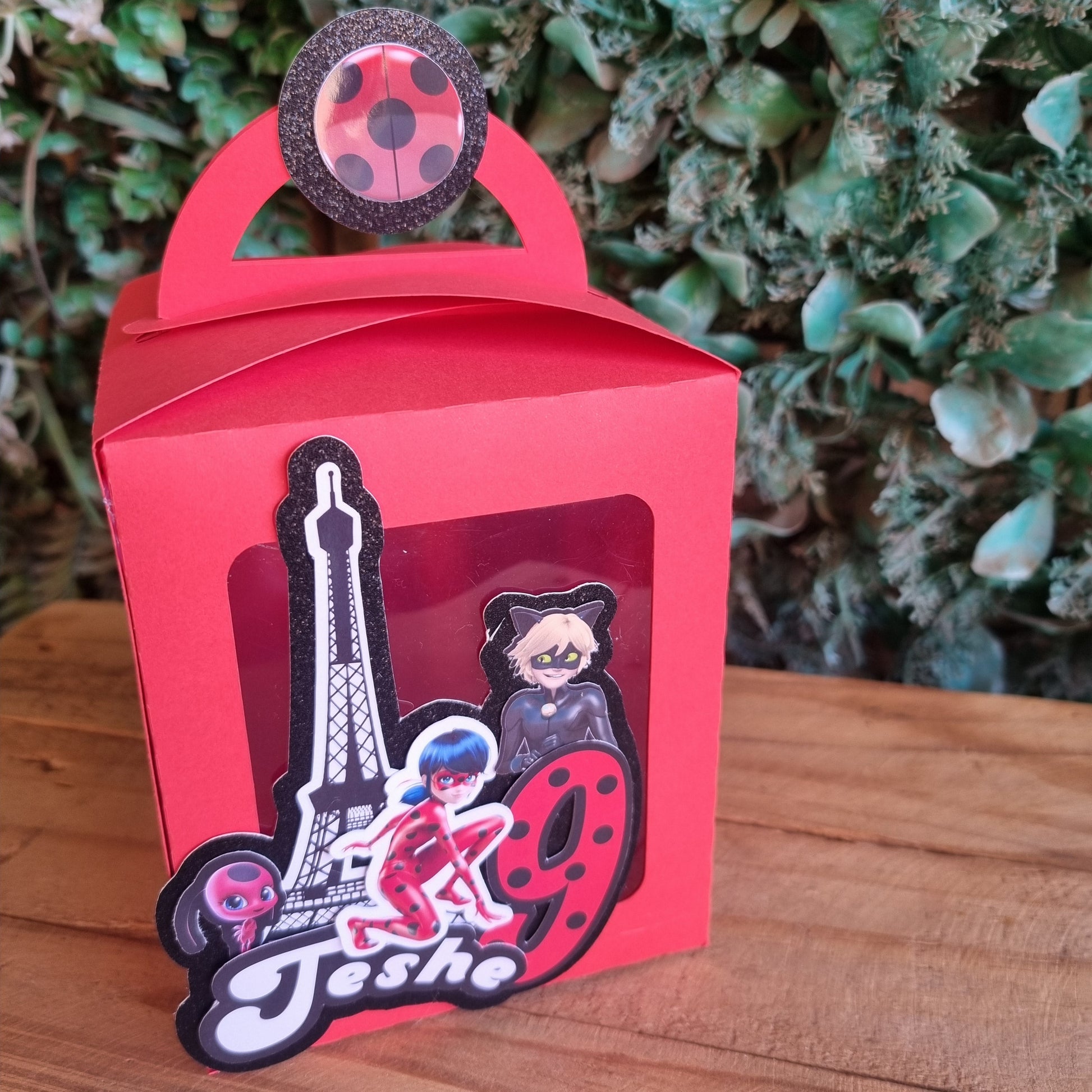Red mug-shaped box with a decorative item on a wooden surface and green foliage background