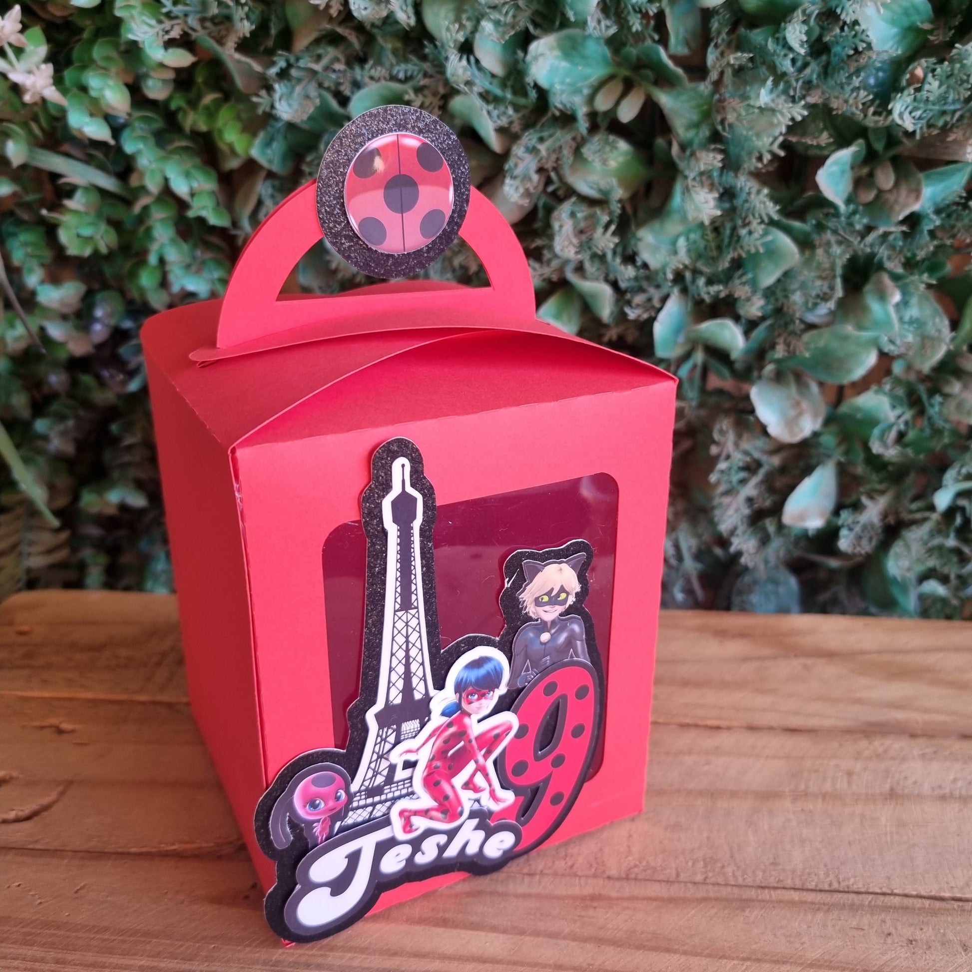 Red gift box with decorative elements on a wooden surface and green foliage background
