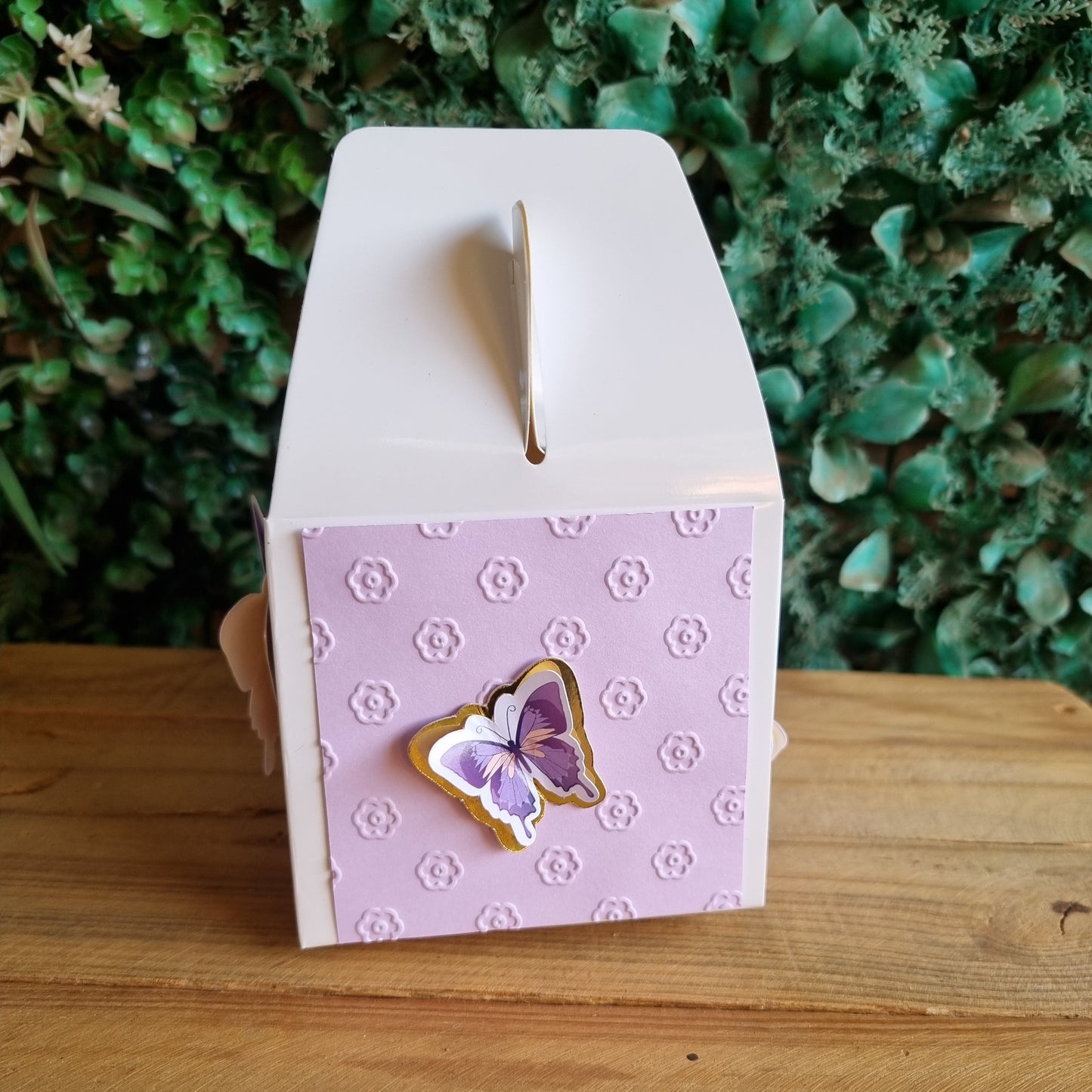Small purple card with a butterfly design attached to a white mailbox against a wooden and green background