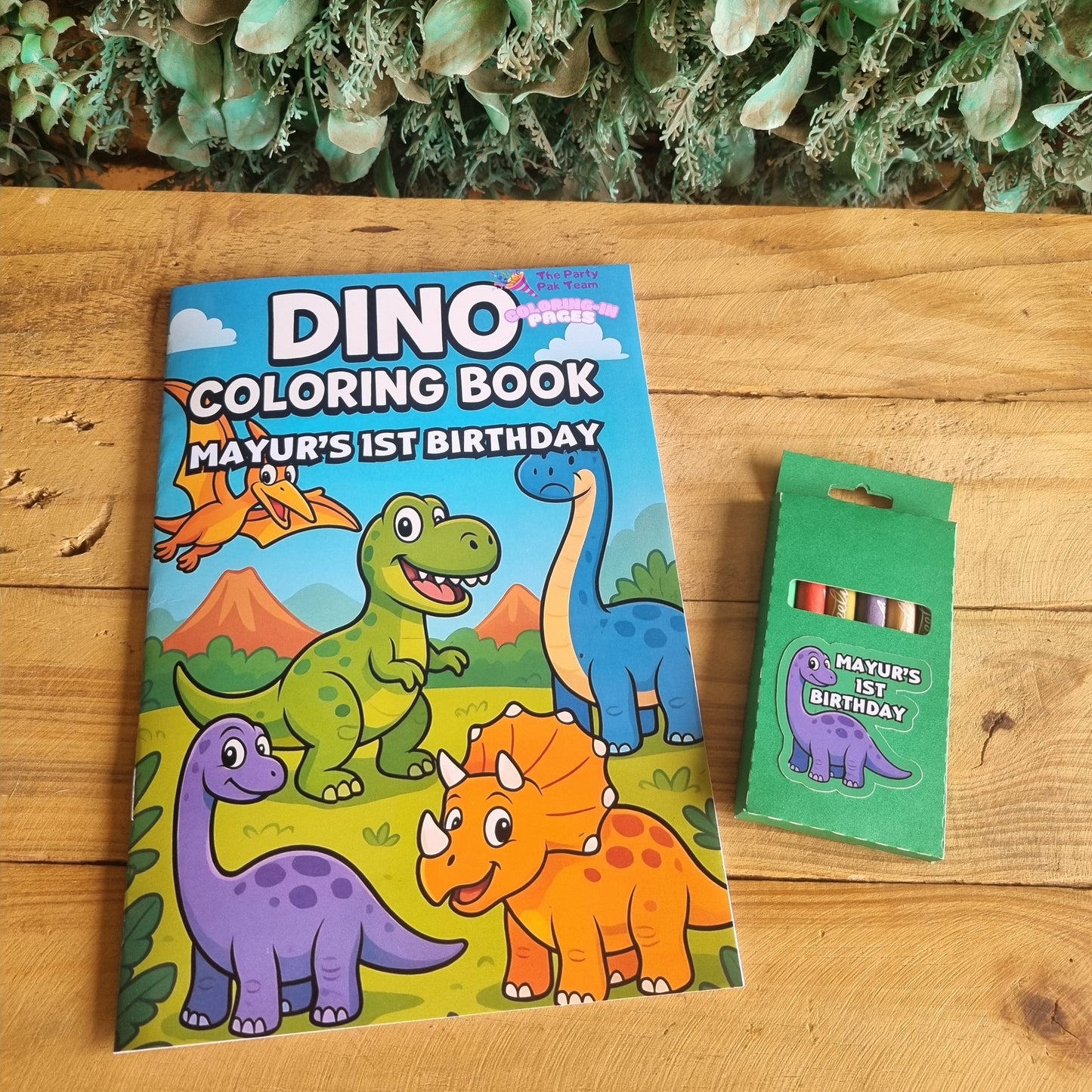 Dinosaur coloring book and crayons on a wooden surface with greenery.