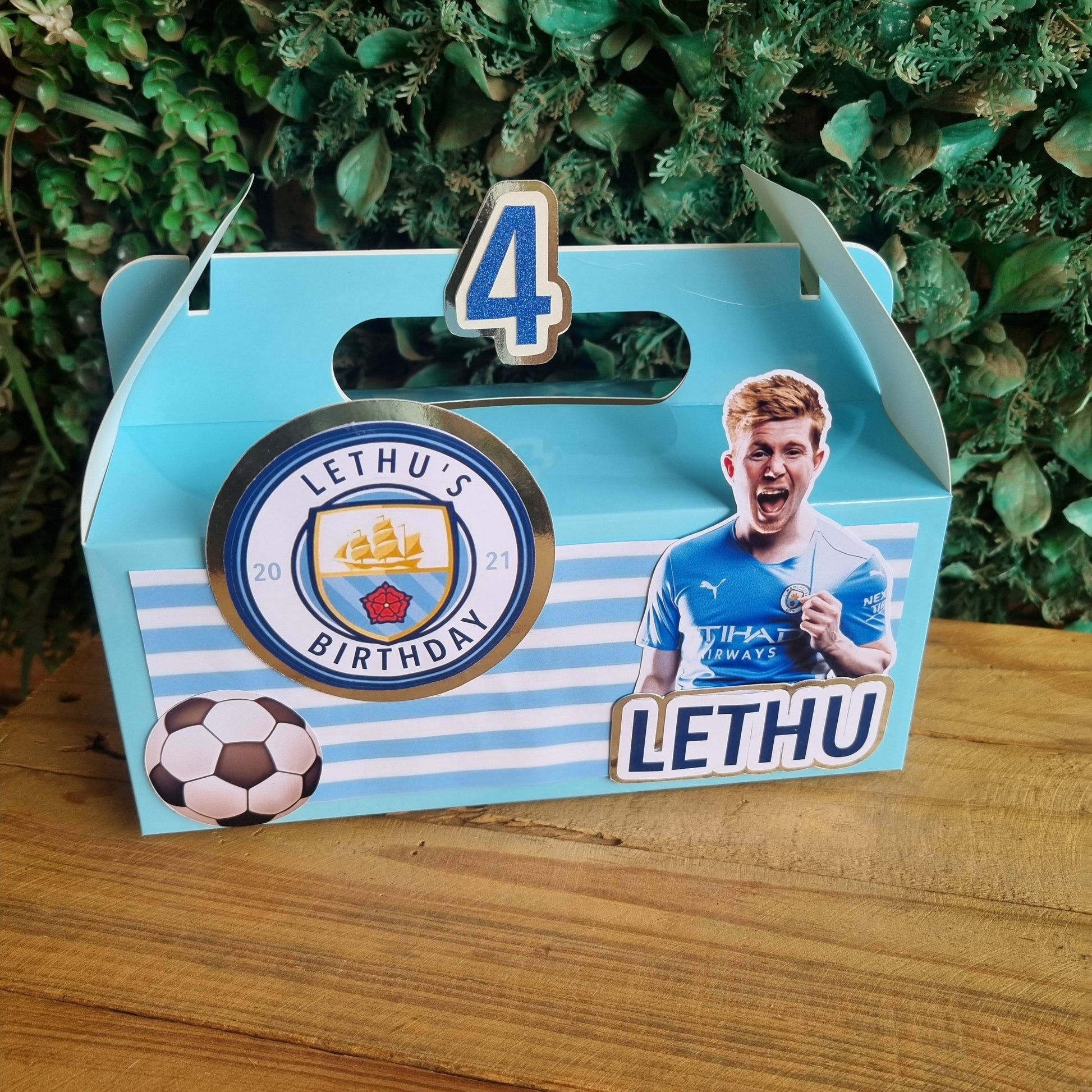 Card with a soccer player and Lethu branding on a wooden surface with greenery.