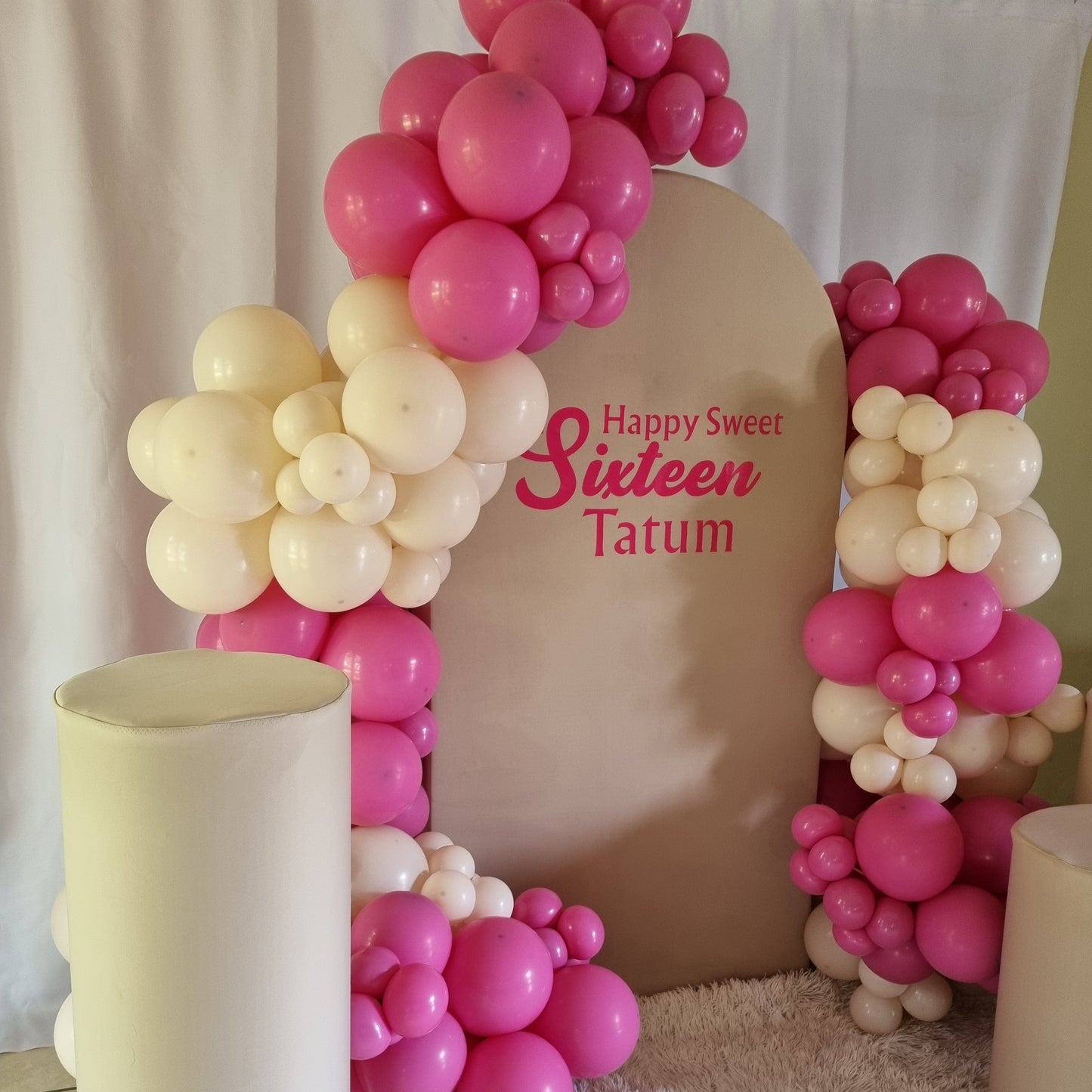 Decorative arch made of pink and white balloons with 'Happy Sweet Sixteen' text on a cushion.