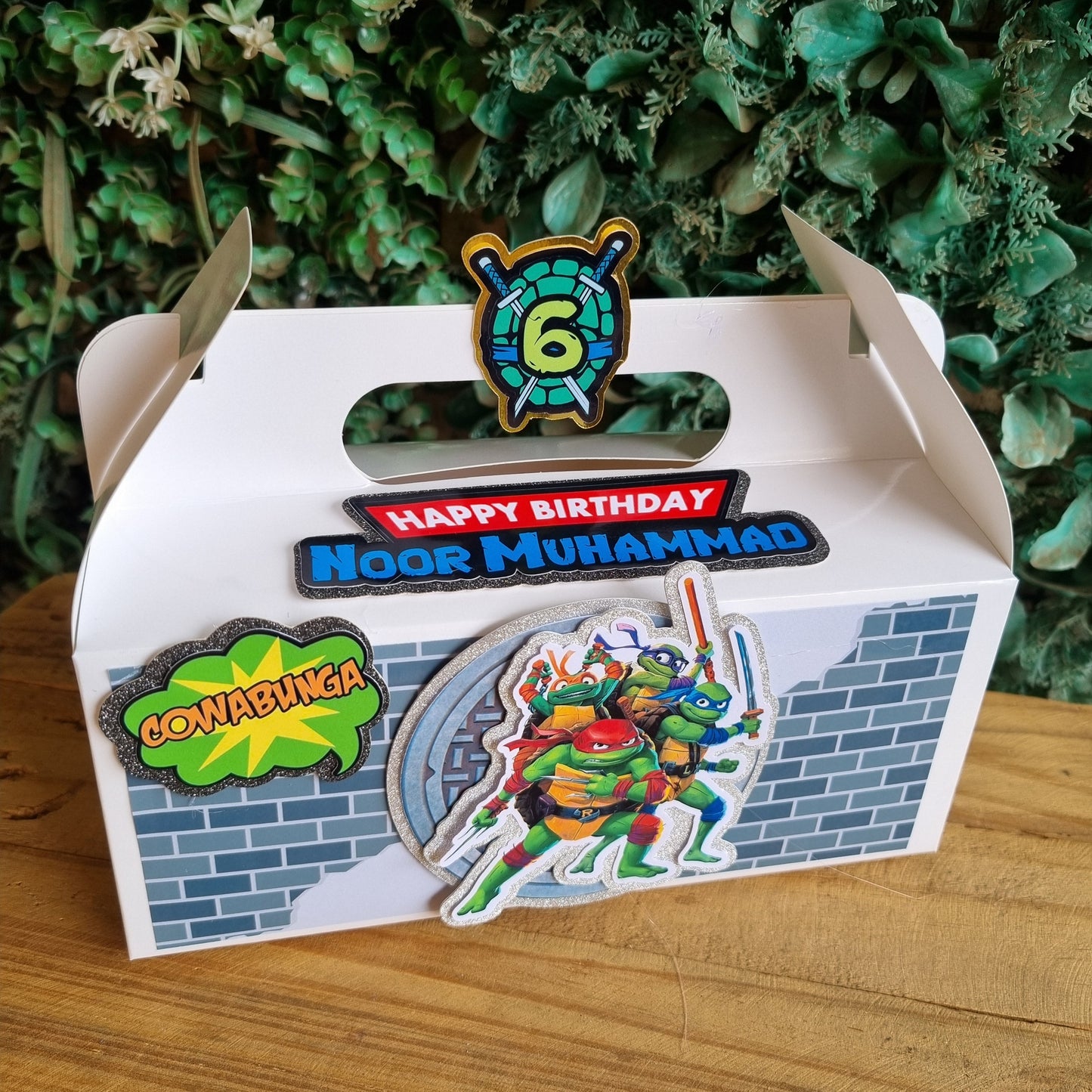 Cardboard cutout of a birthday cake with colorful decorations on a wooden surface.