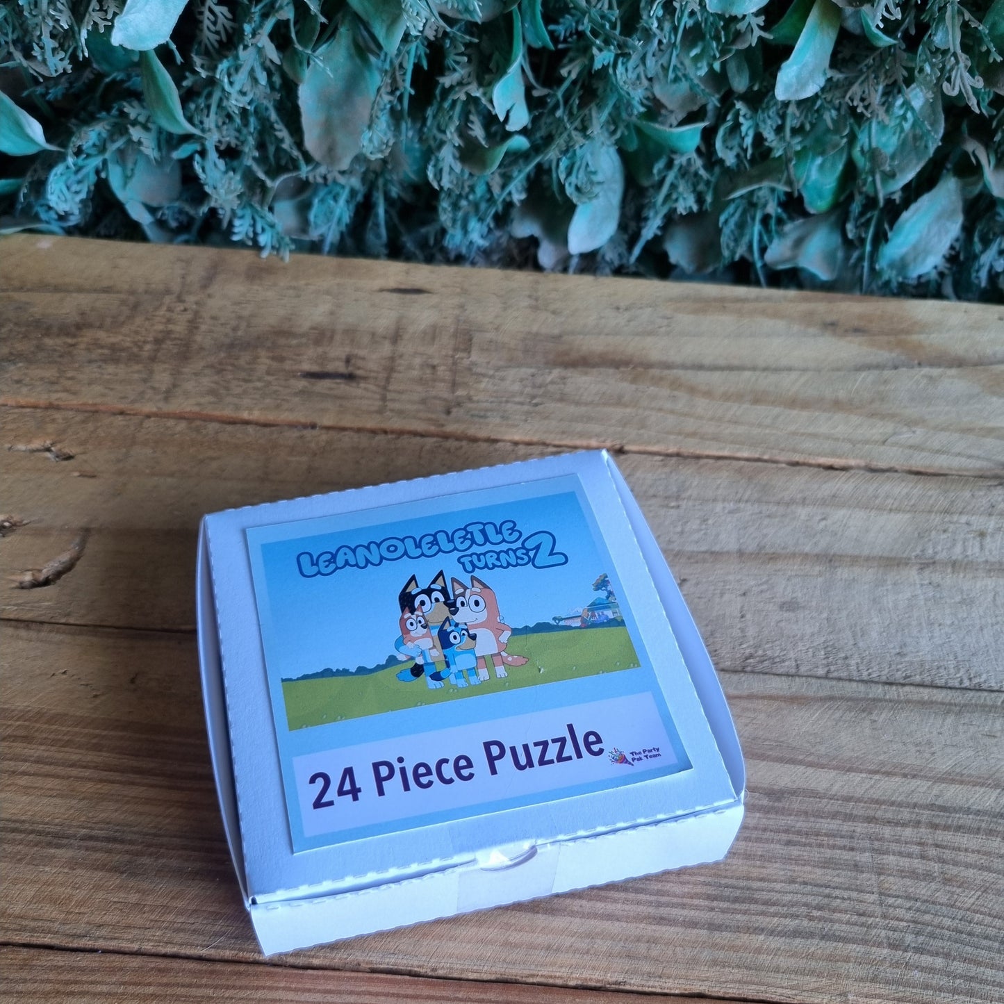 24 piece puzzle box on a wooden surface with greenery in the background