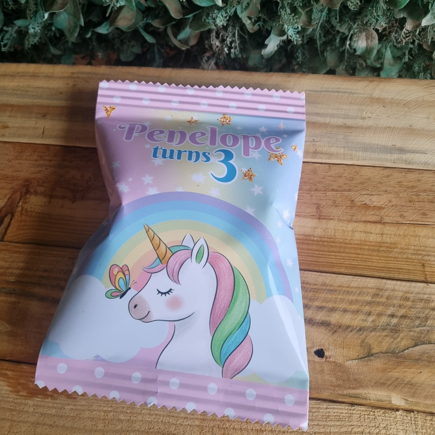 Unicorn-themed snack package on a wooden surface with greenery in the background