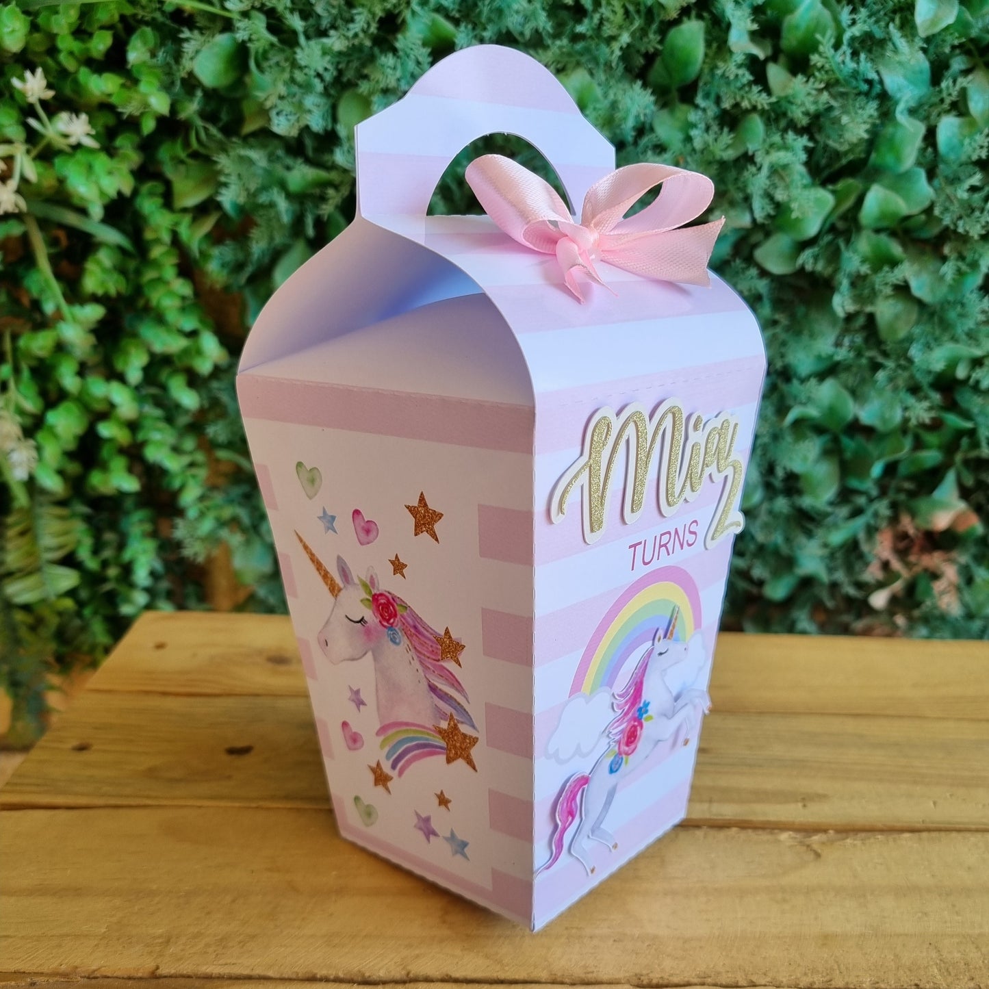 Decorative pink box with unicorn design on grass and wooden surface
