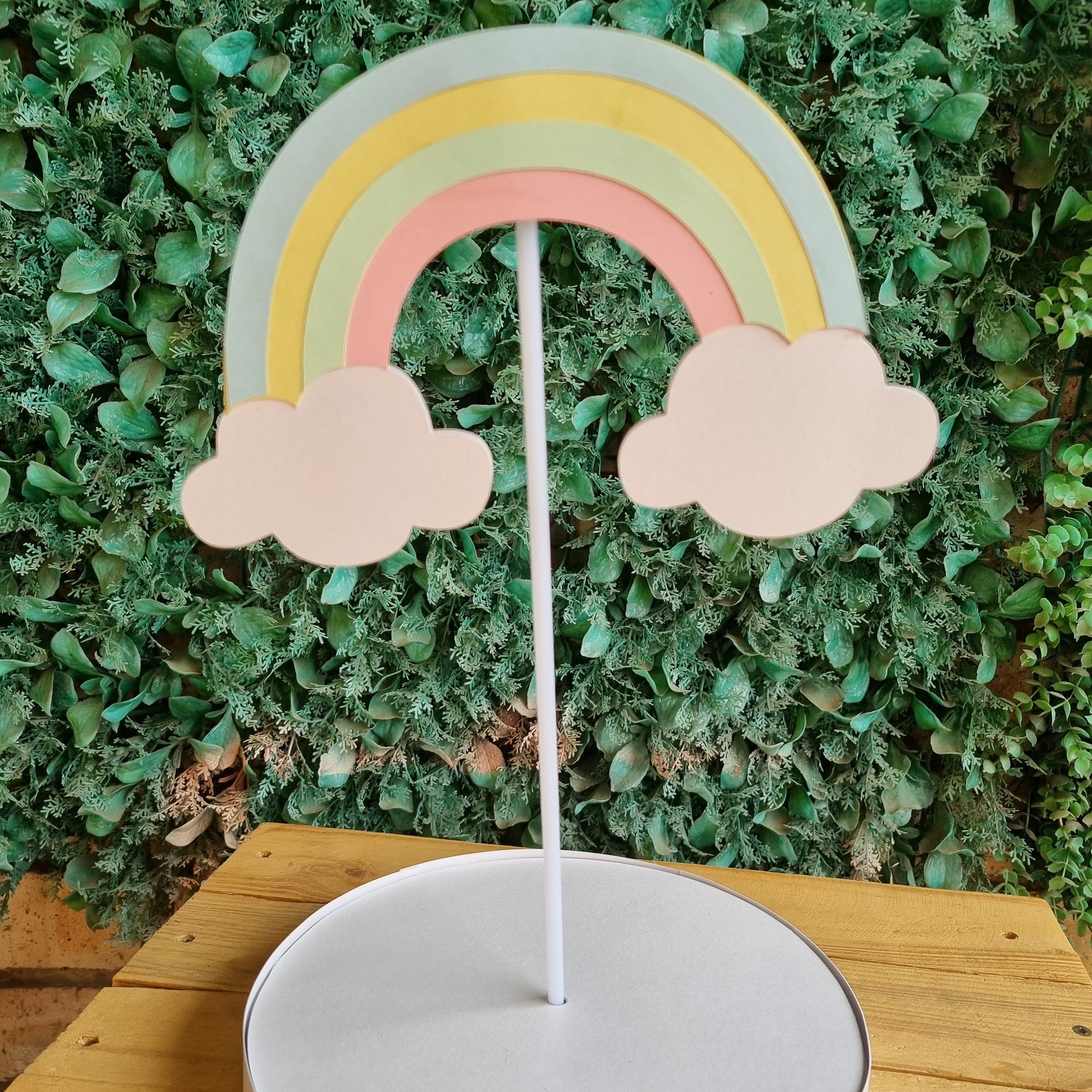 Decorative wall clock with a rainbow and cloud design on a grassy background