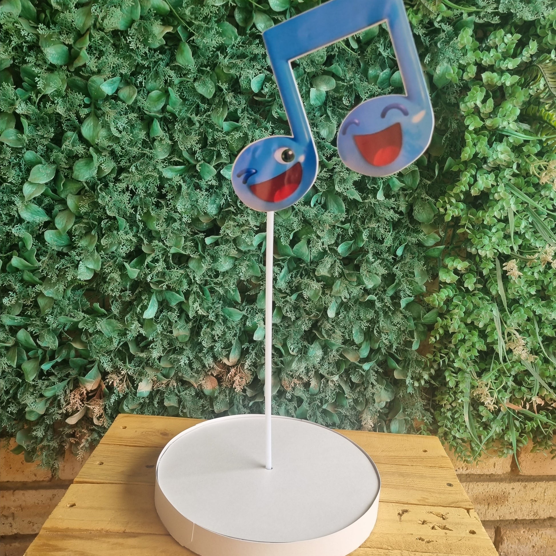 Blue and red bird-shaped object attached to a white circular device against a green bush background.