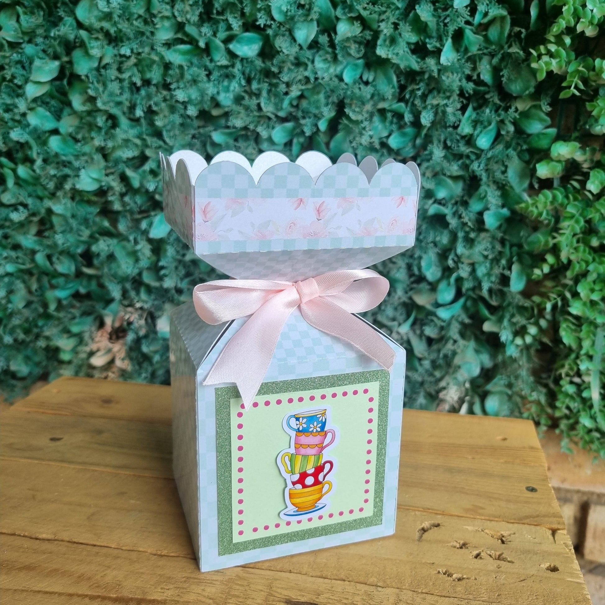 Gift box with a bow on a wooden surface with greenery in the background