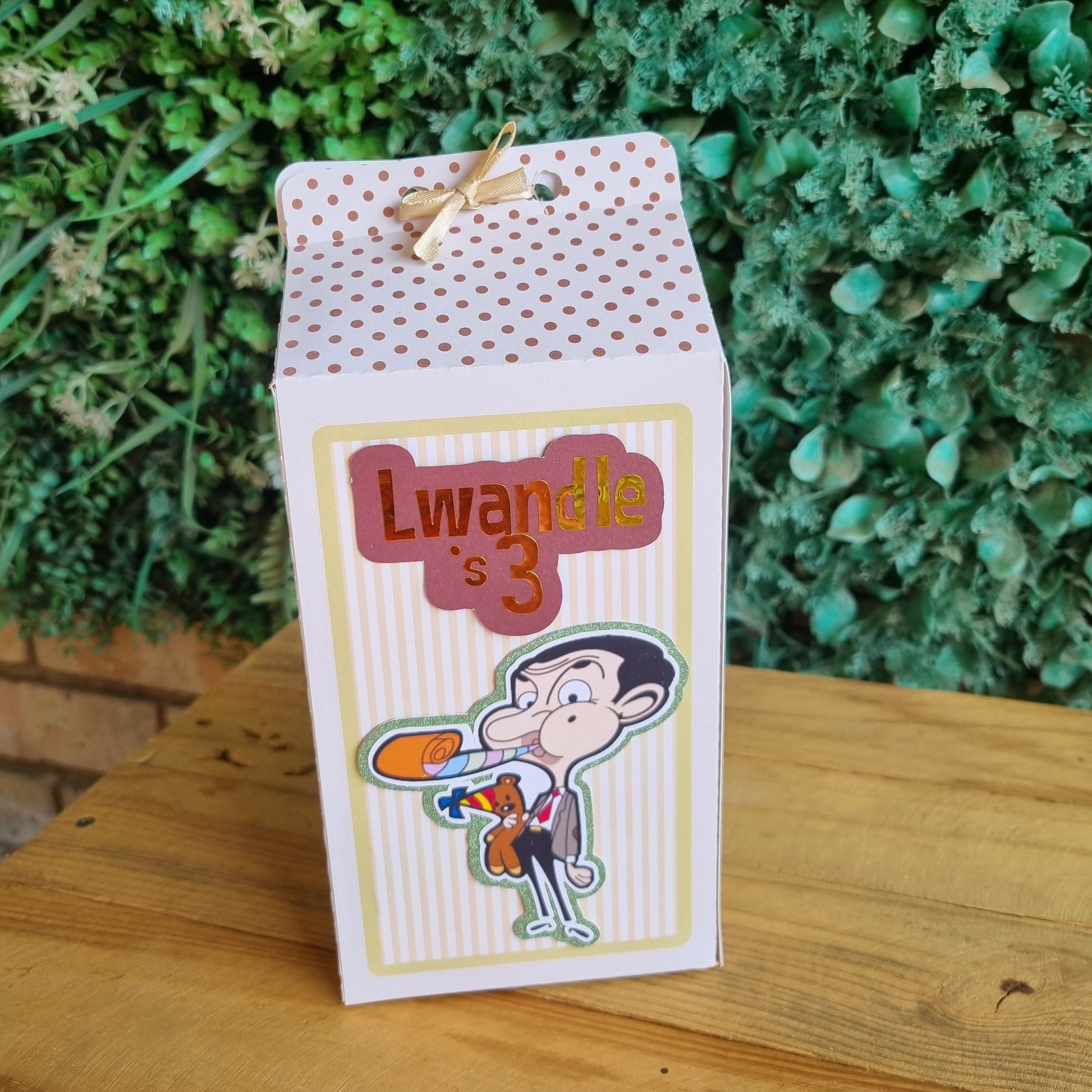 Gift bag with cartoon character and text 'Lwandle is 3' against a green leafy background