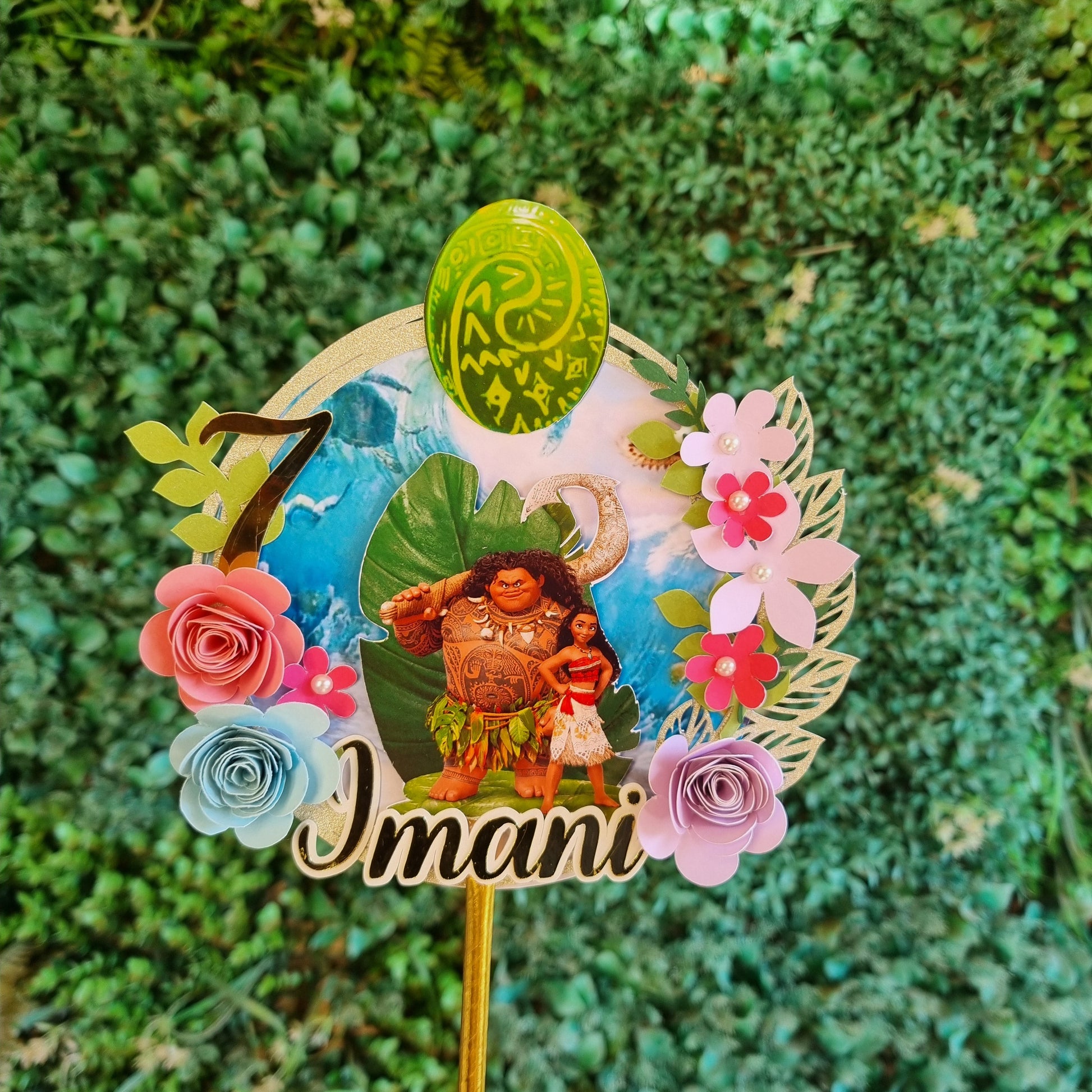 Decorative hair stick with flowers and 'Imani' text on a green leafy background