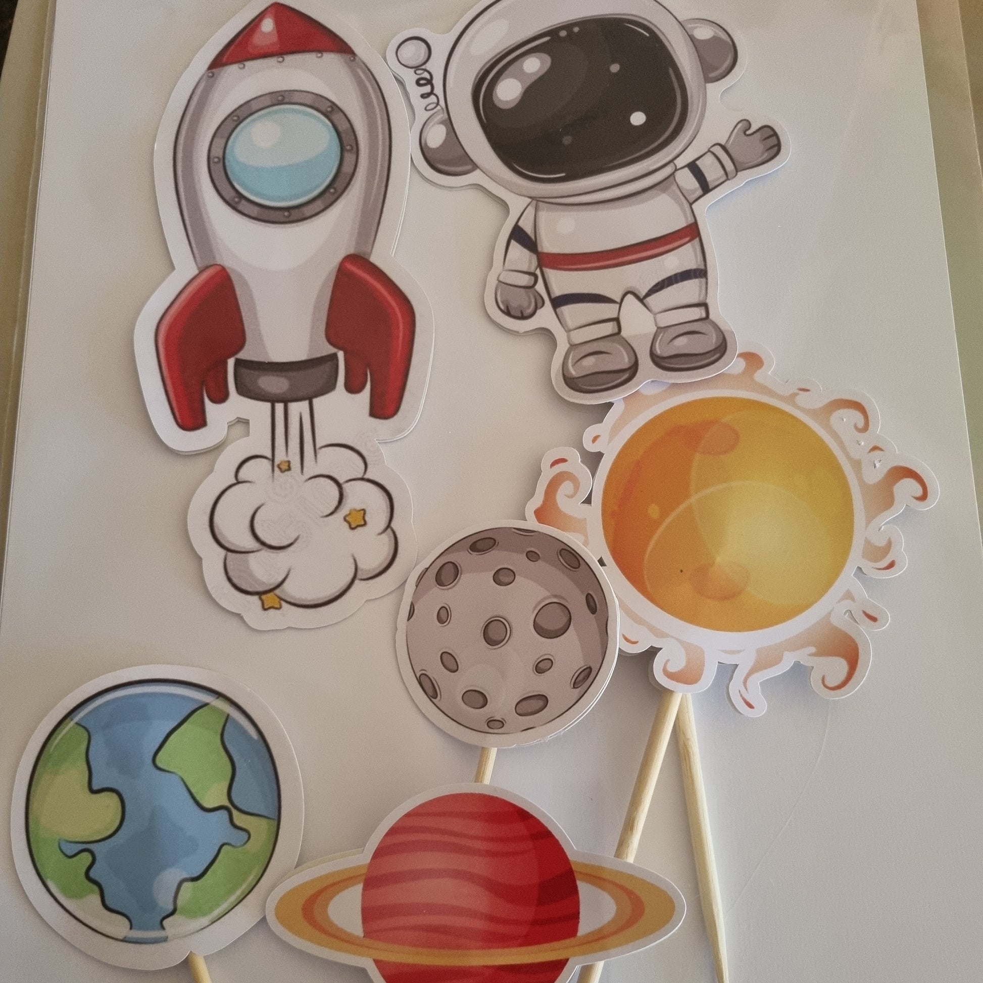 Solar system-themed cutouts on sticks with a space helmet, sun, moon, planet, rocket, and Earth.