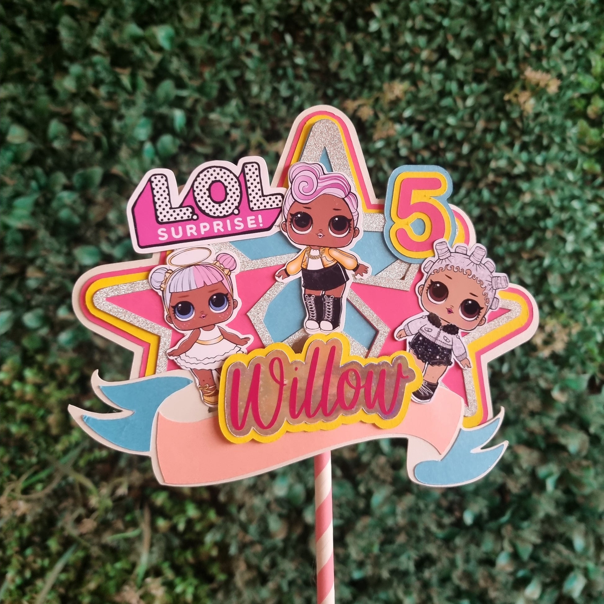Colorful 'Lol Dolls' toy figure on a stick against a green leafy background