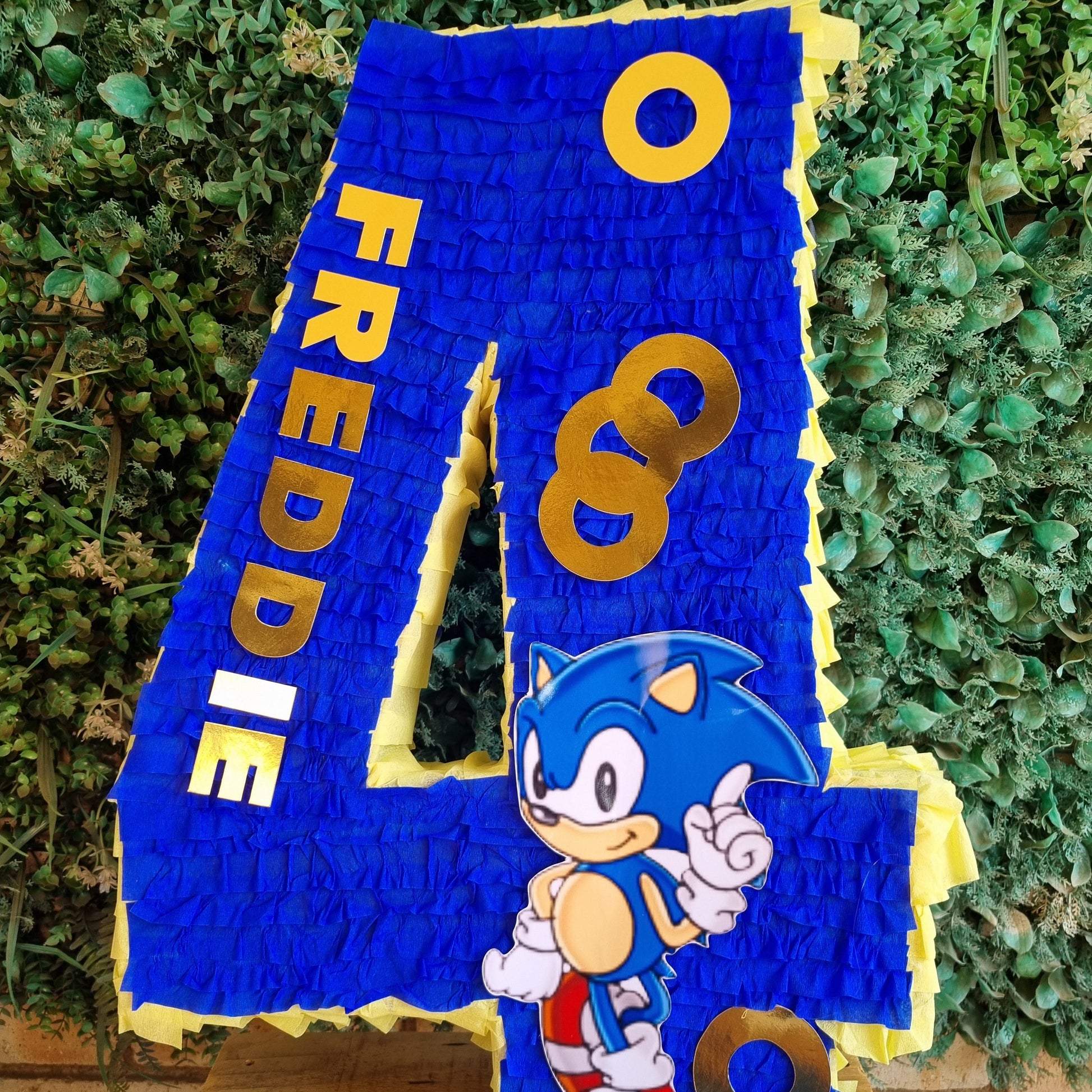 Blue piñata shaped like the number '4' with a character on it, against a green leafy background.