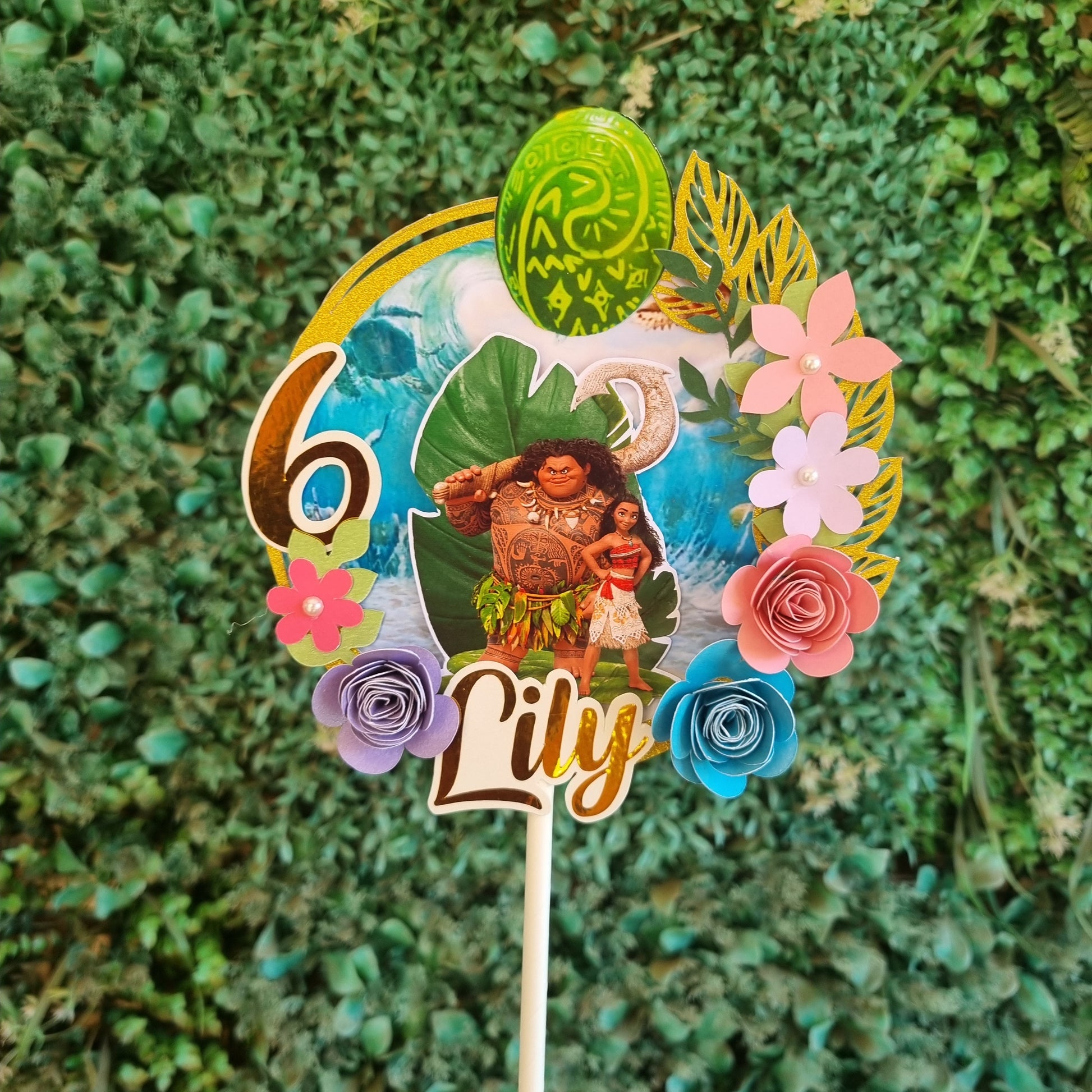 Decorative hair stick with flowers and 'Nily' text on a green grass background