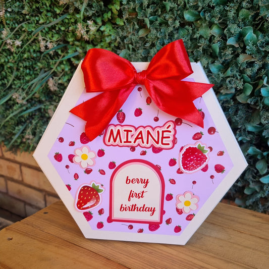 Hexagonal card with red ribbon, strawberry design, and 'MIANE' branding on a wooden surface.