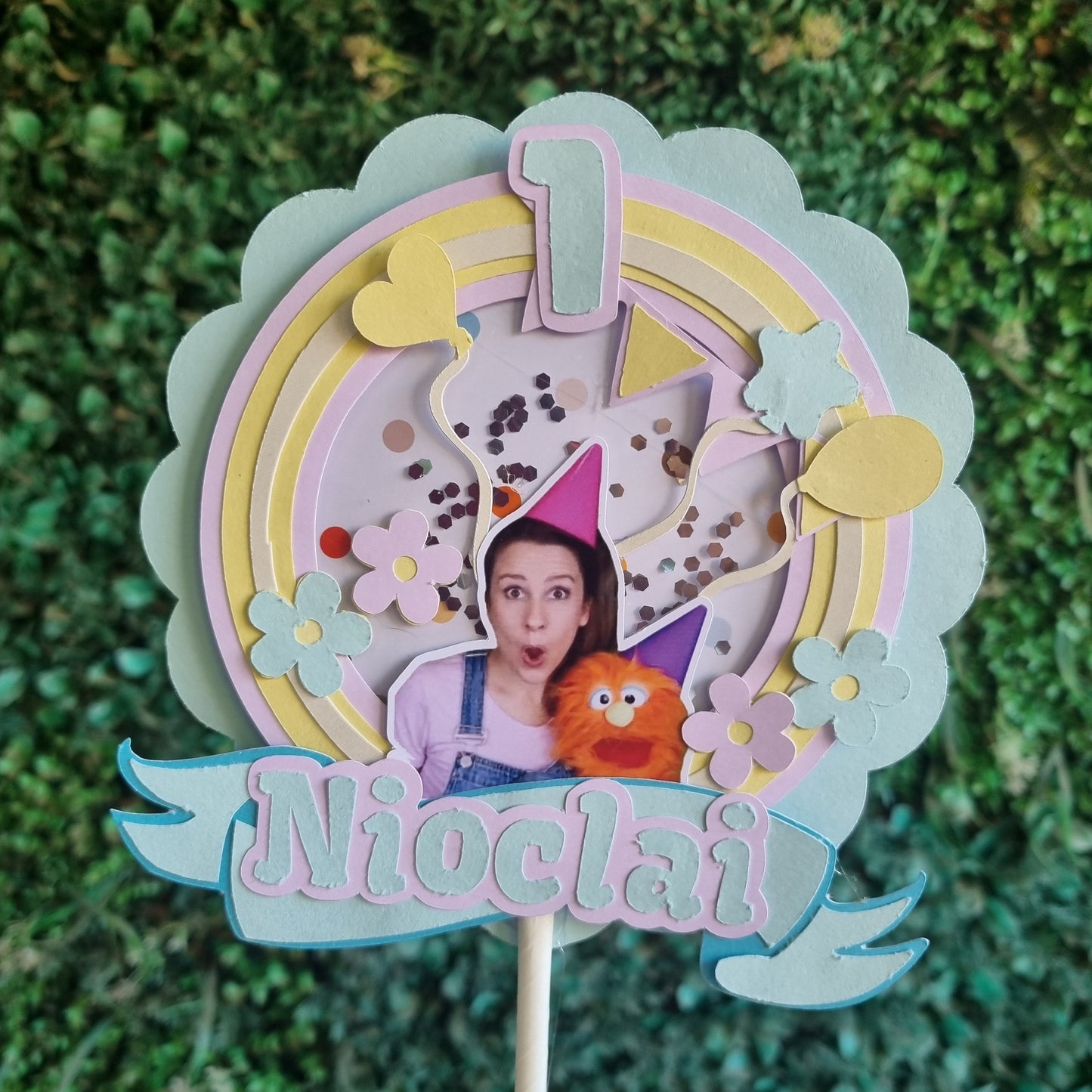Colorful decorative item with a character and the name 'Nicola' on a green textured background