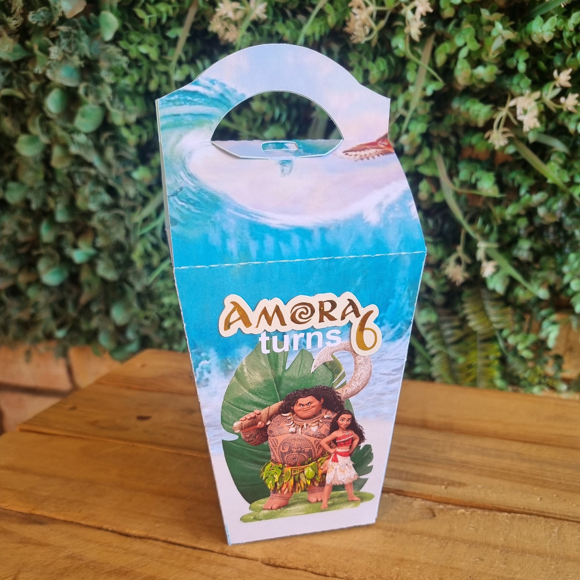 Amora product packaging on a wooden surface with greenery in the background