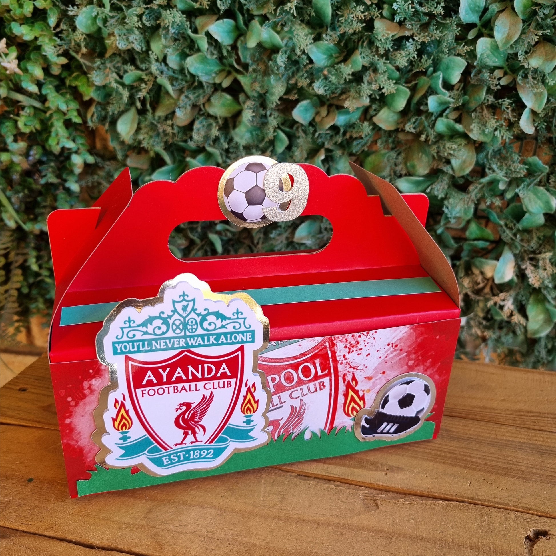Red toy truck with a football design on a wooden surface and green grass background