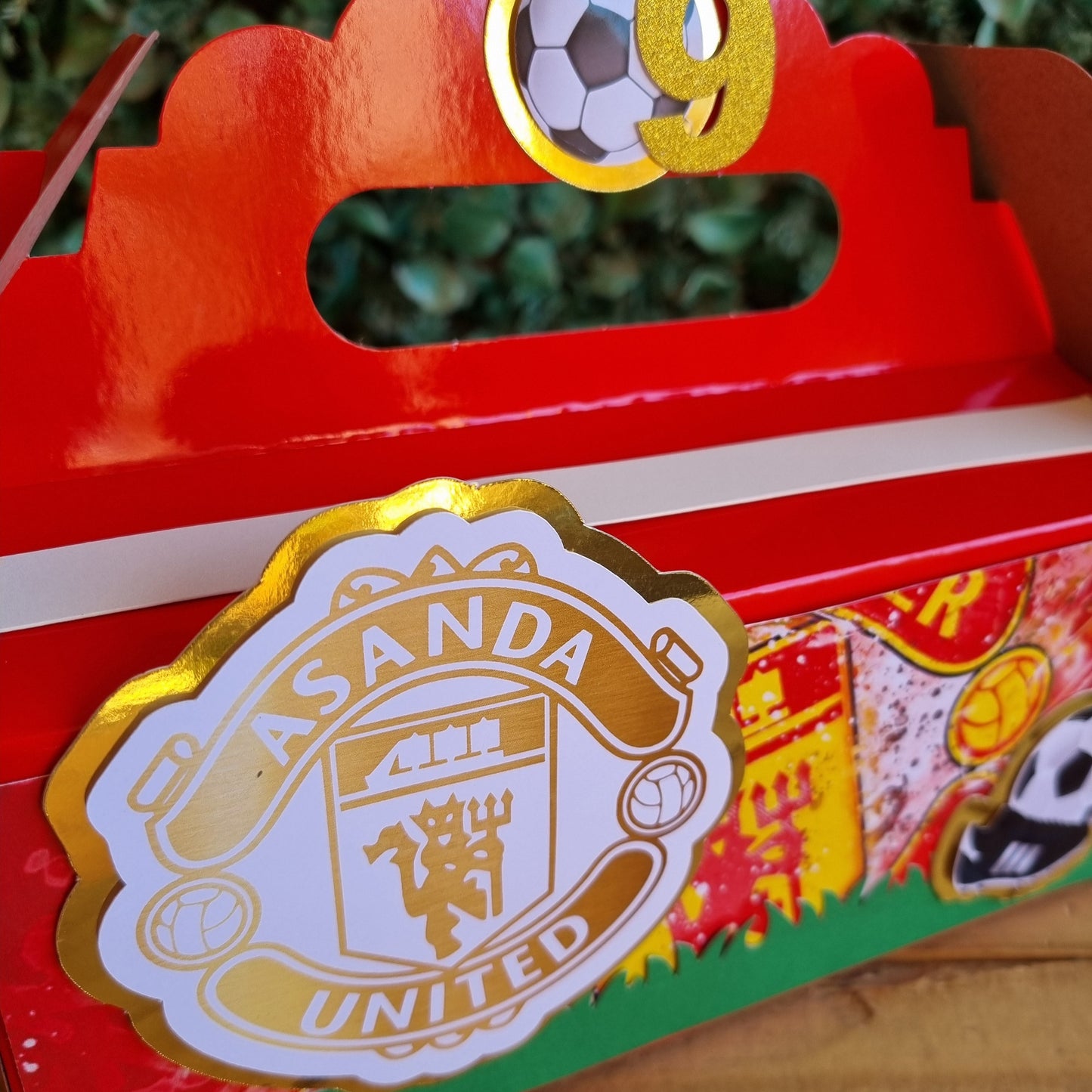 Red gift box with a gold and white logo on a wooden surface