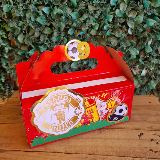Red decorative item with gold and white design on a wooden surface and green foliage background