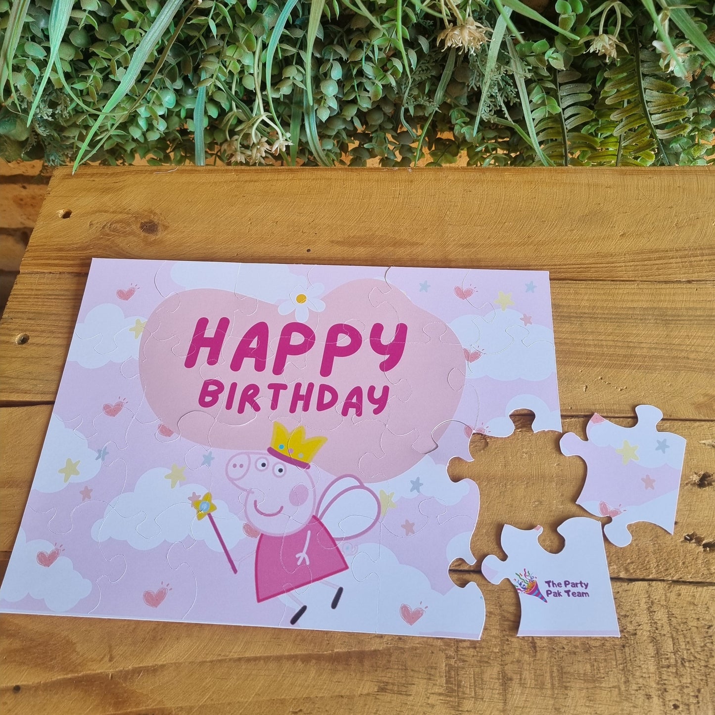 Happy Birthday card with a pig design on a wooden surface with greenery.