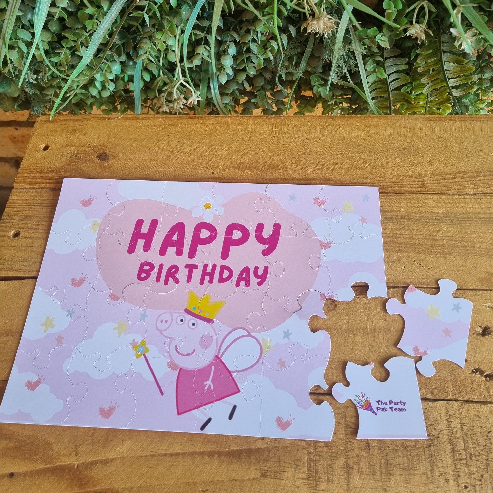 Happy Birthday card with a pig design on a wooden surface with greenery.