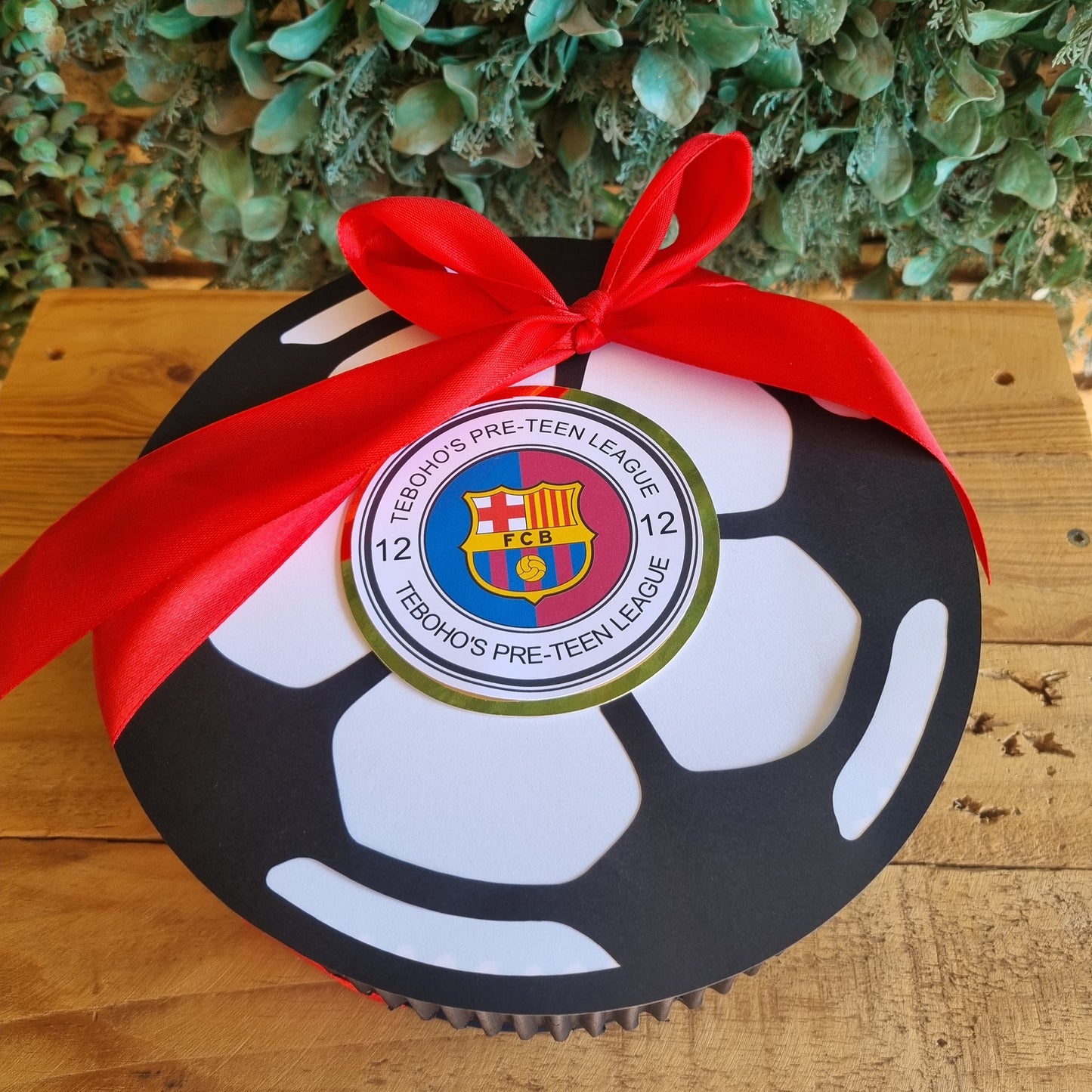 Decorative reel with a red ribbon and emblem on a wooden surface with greenery.