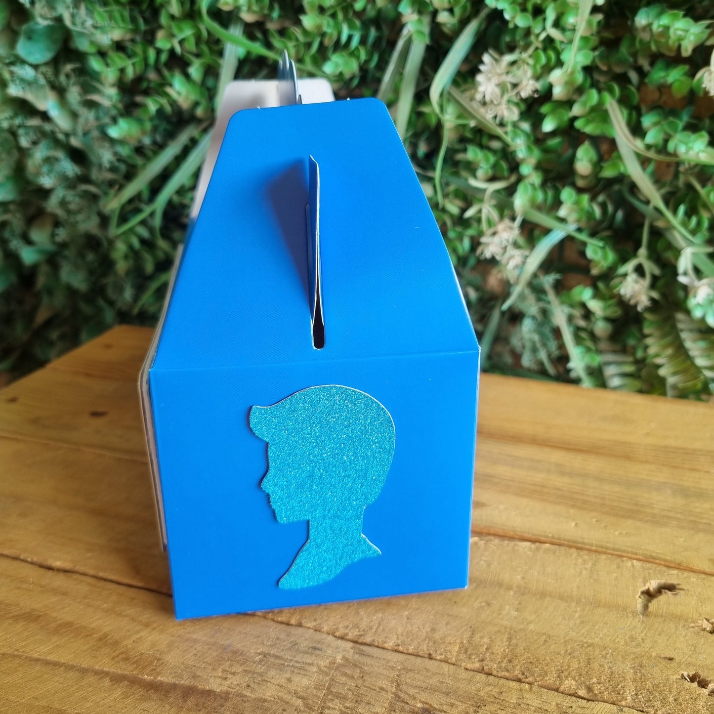 Blue mailbox with whale design on a wooden surface and greenery background