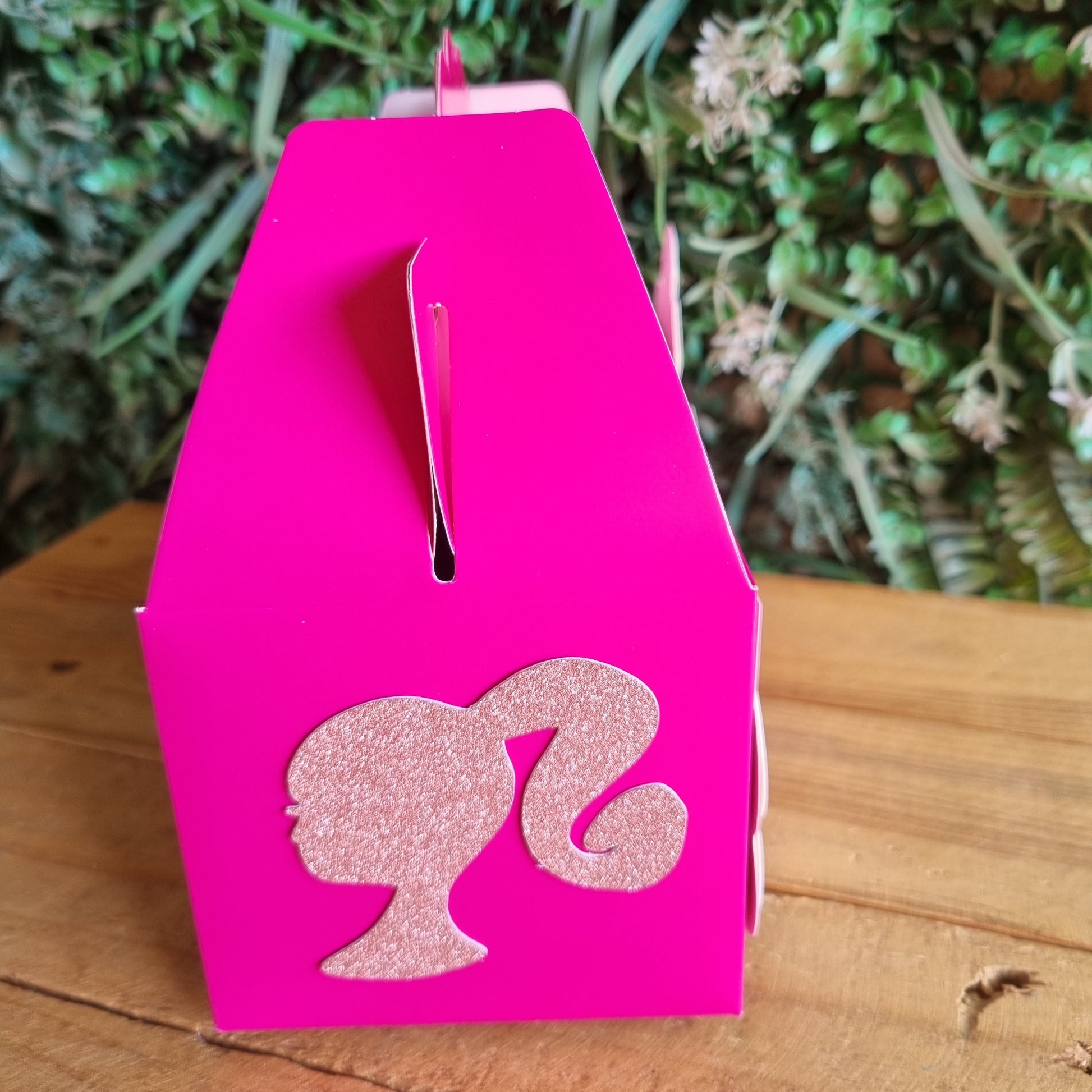 Pink card with a fish design on a wooden surface and green plants in the background