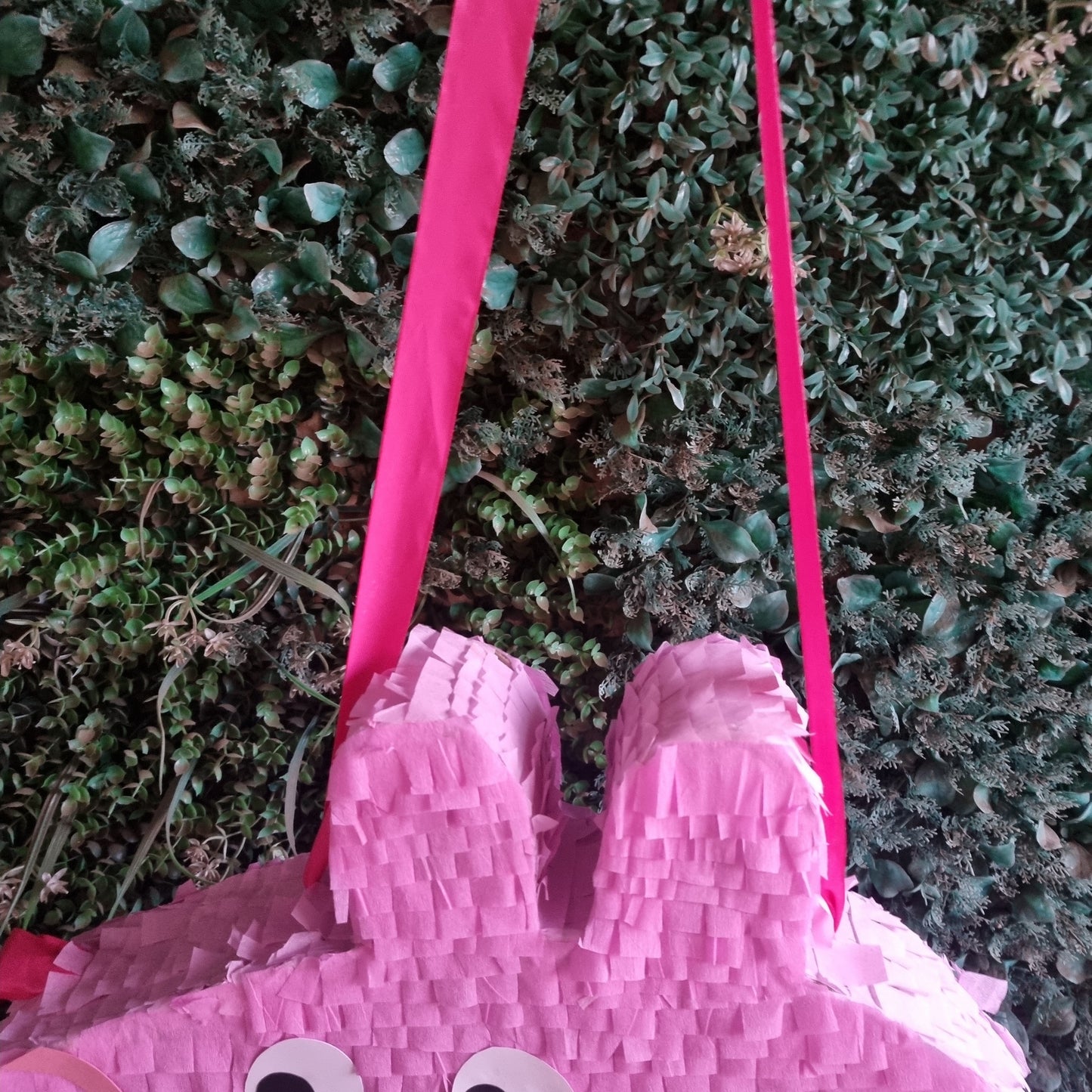 Pink pig-shaped pinata with a pink ribbon on grass