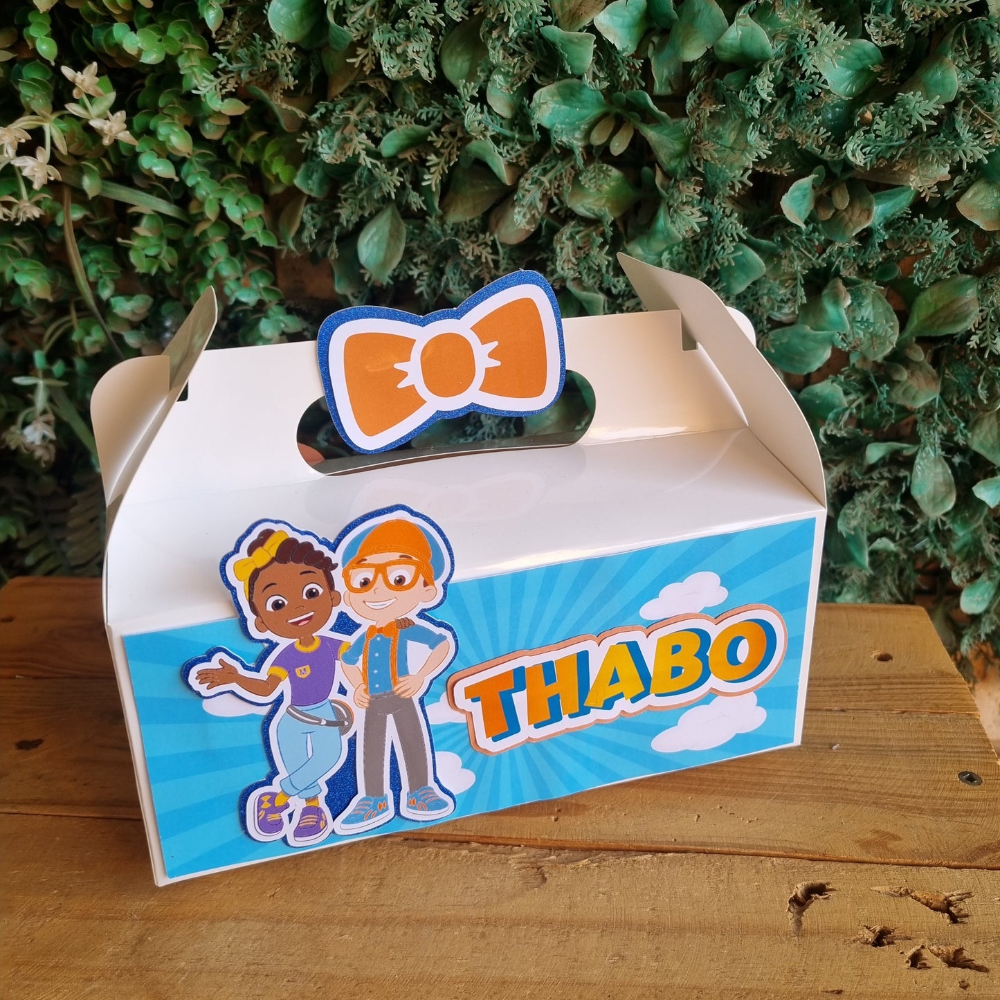 Cartoon character-themed mailbox with 'THABO' branding against a wooden and green leafy background