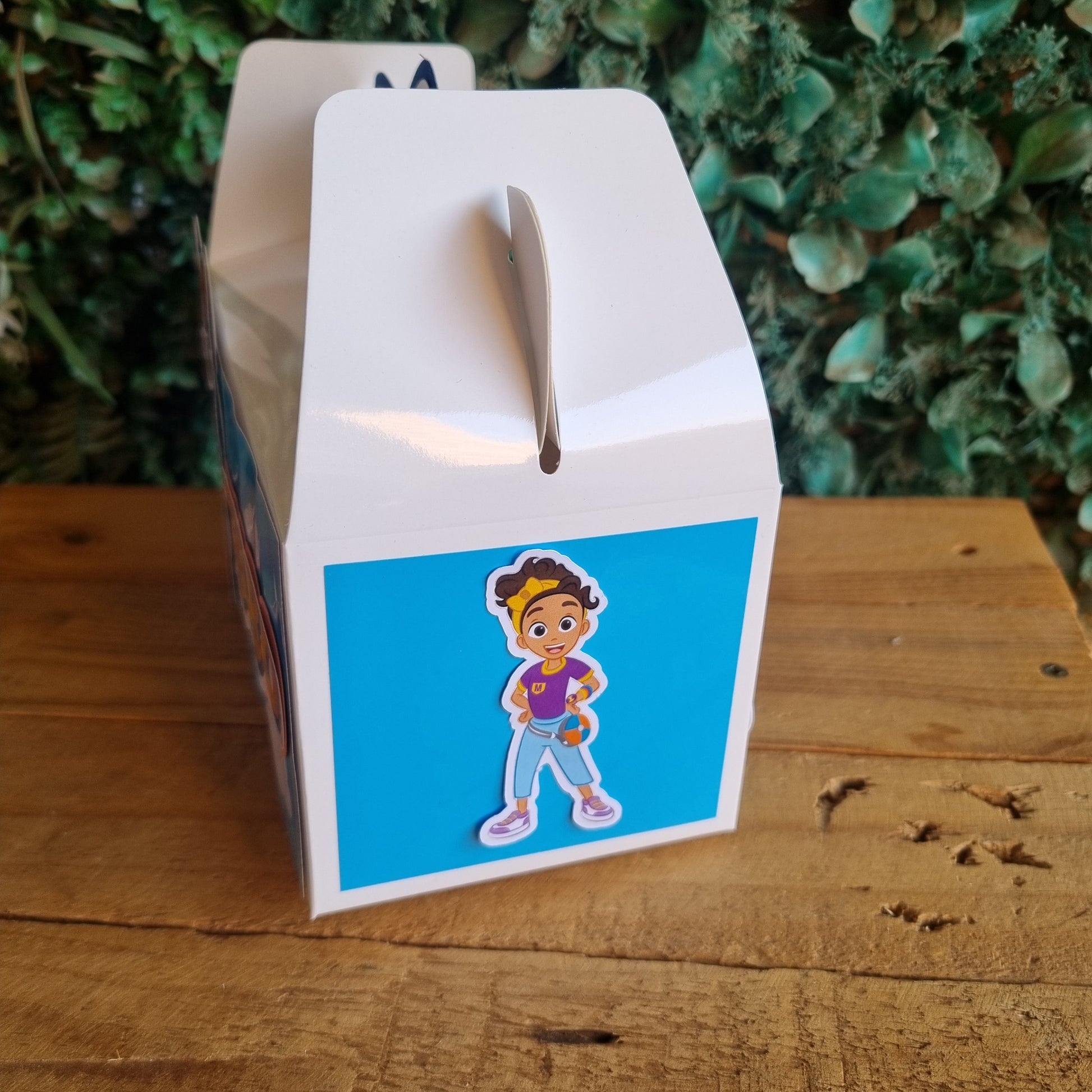 Card with a cartoon character on a blue background, placed on a wooden surface with greenery in the background.