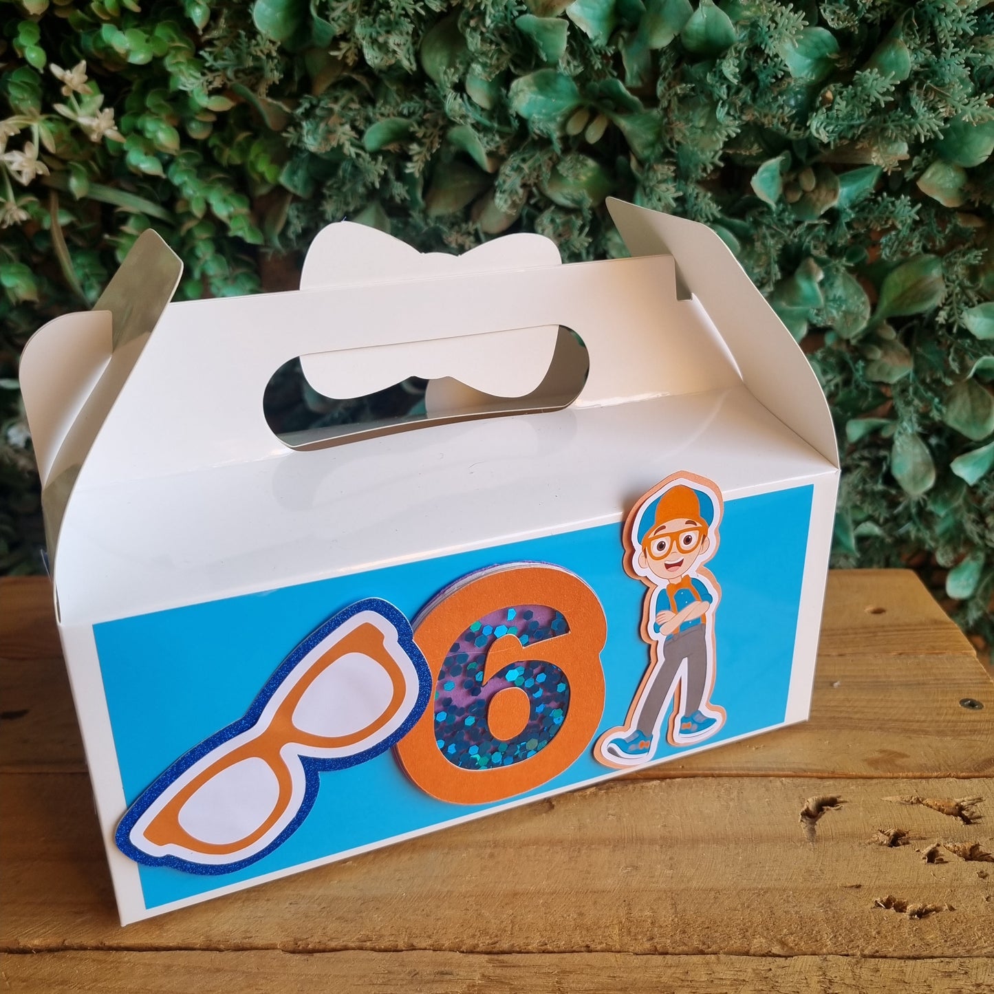 Colorful mailbox with cartoon face design against a wooden and green leafy background