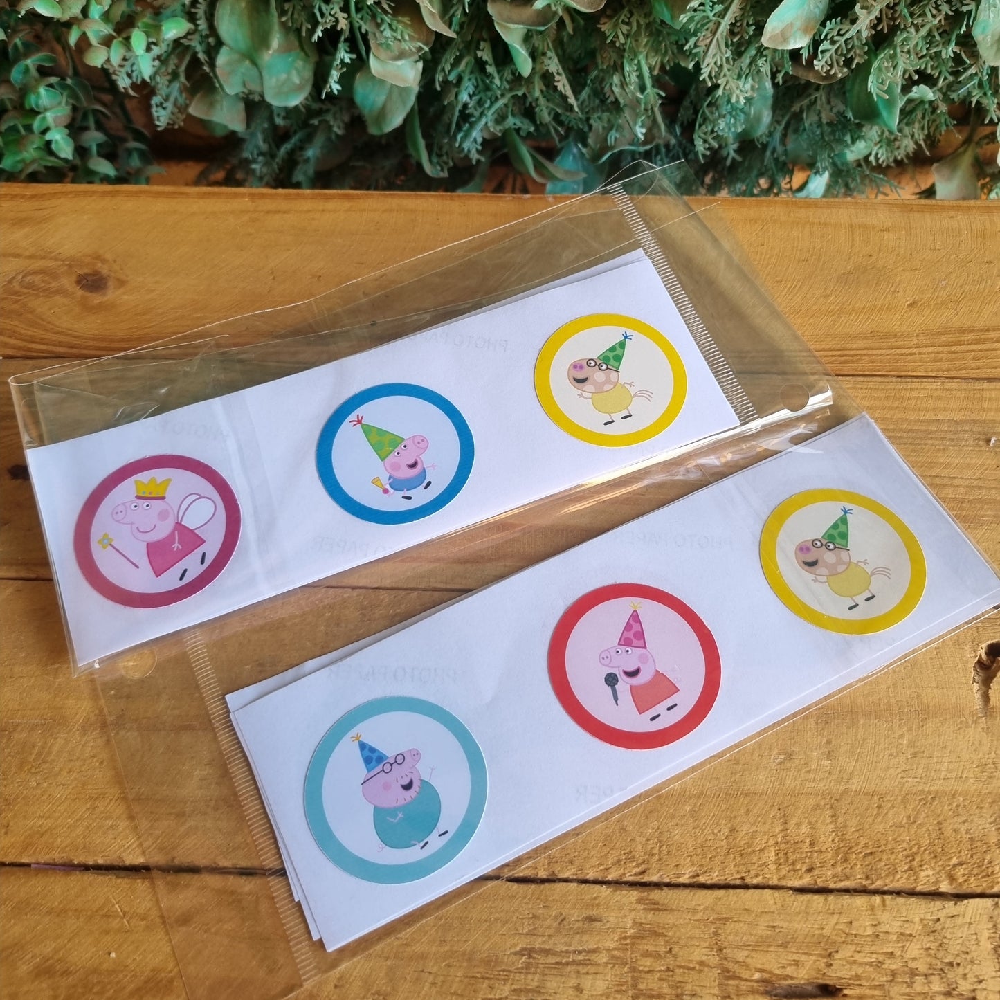 Two sheets of colorful stickers on a wooden surface with greenery in the background