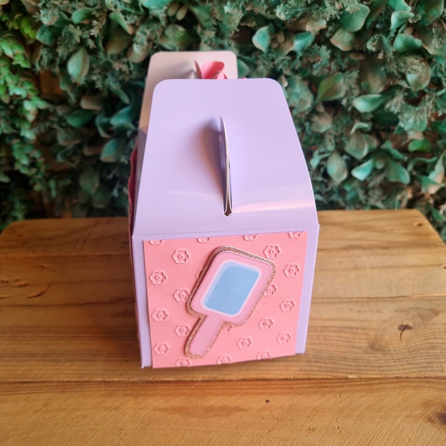 Pink and purple mailbox with a blue label attached to a wooden post.