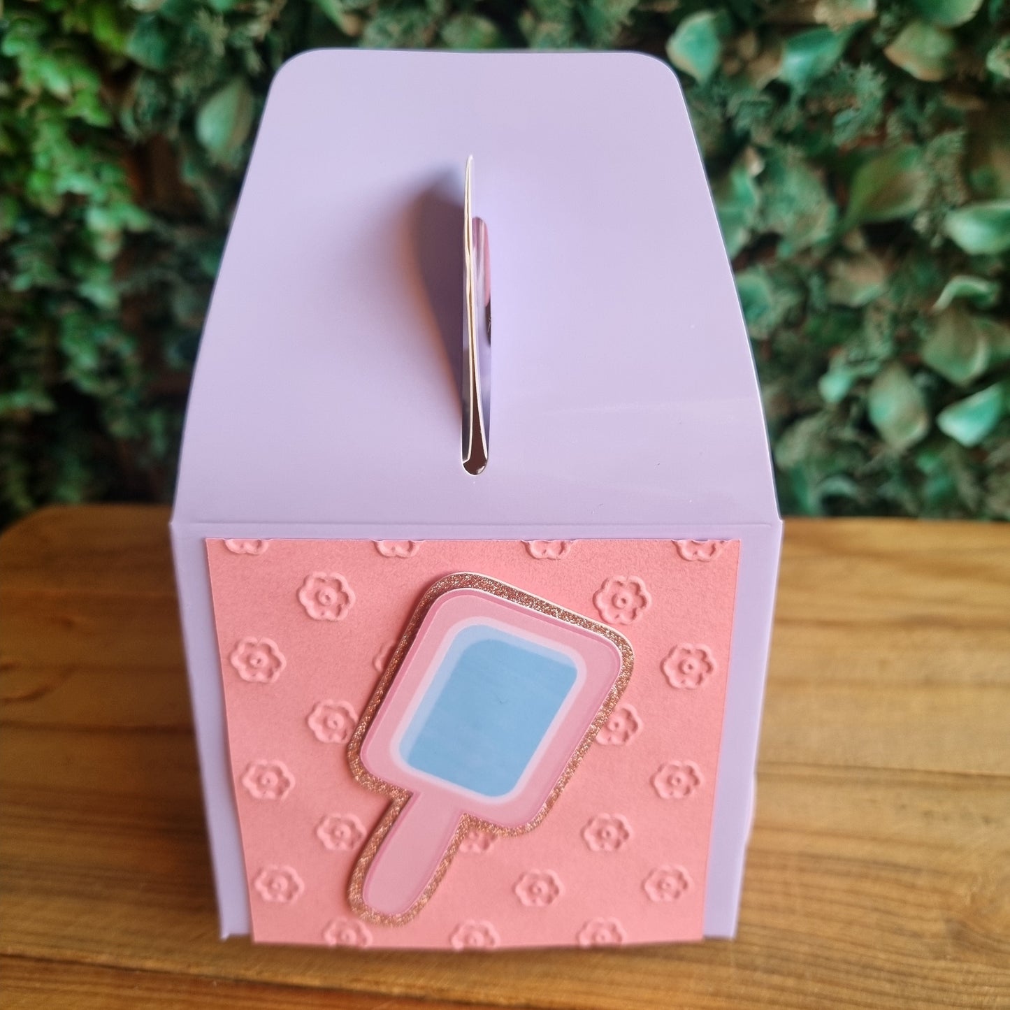 Small pink and white box with a blue gem-like object on a wooden surface.